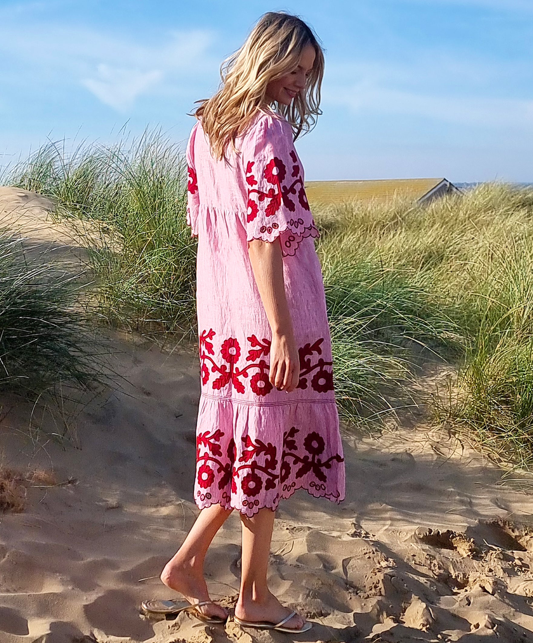 Back view of model stood in sand dunes wearing a Rose and Rose red striped linen Agrigento dress.