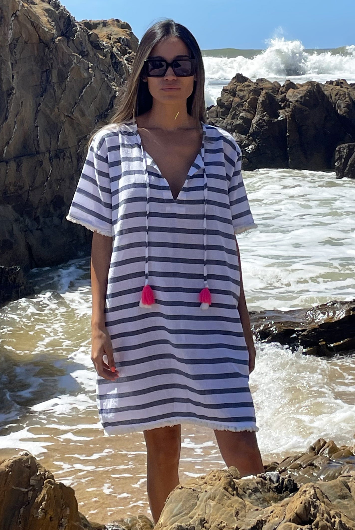 A model standing in front of the sea wearing a Rosebud by Rose and Rose Aix beach dress and sunglasses. 