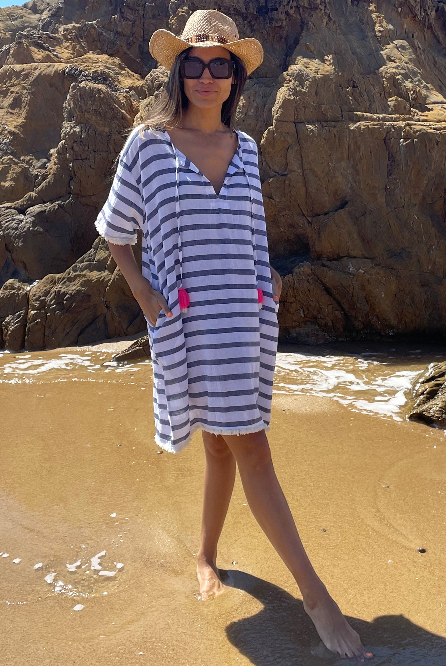 A model standing on the beach wearing a Rosebud by Rose and Rose Aix beach dress, sunglasses and hat. 