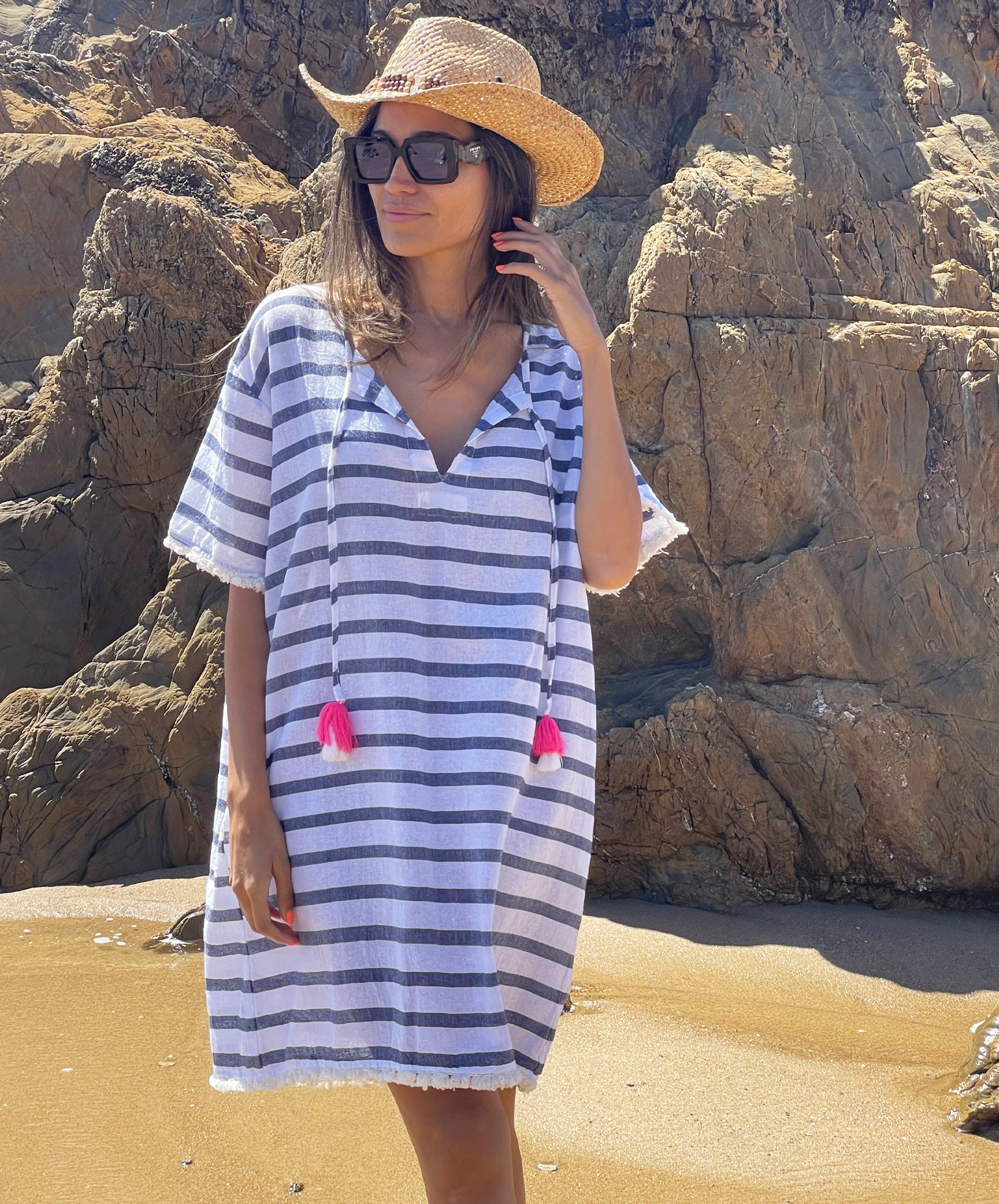 A model standing on the beach wearing a Rosebud by Rose and Rose Aix beach dress, sunglasses and hat. 