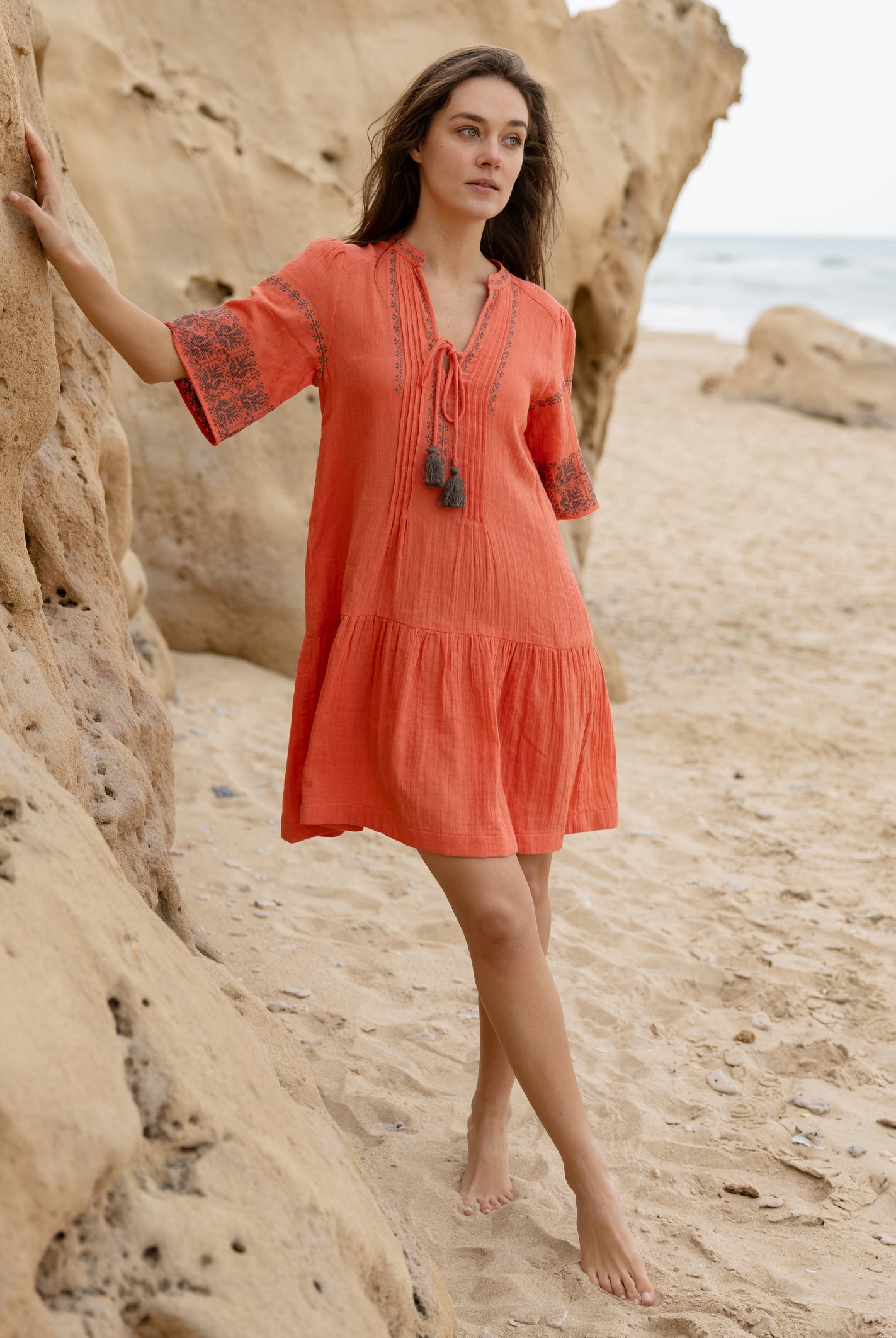 A model wears a Rose and Rose embroidered Ajaccio dress in coral cotton.