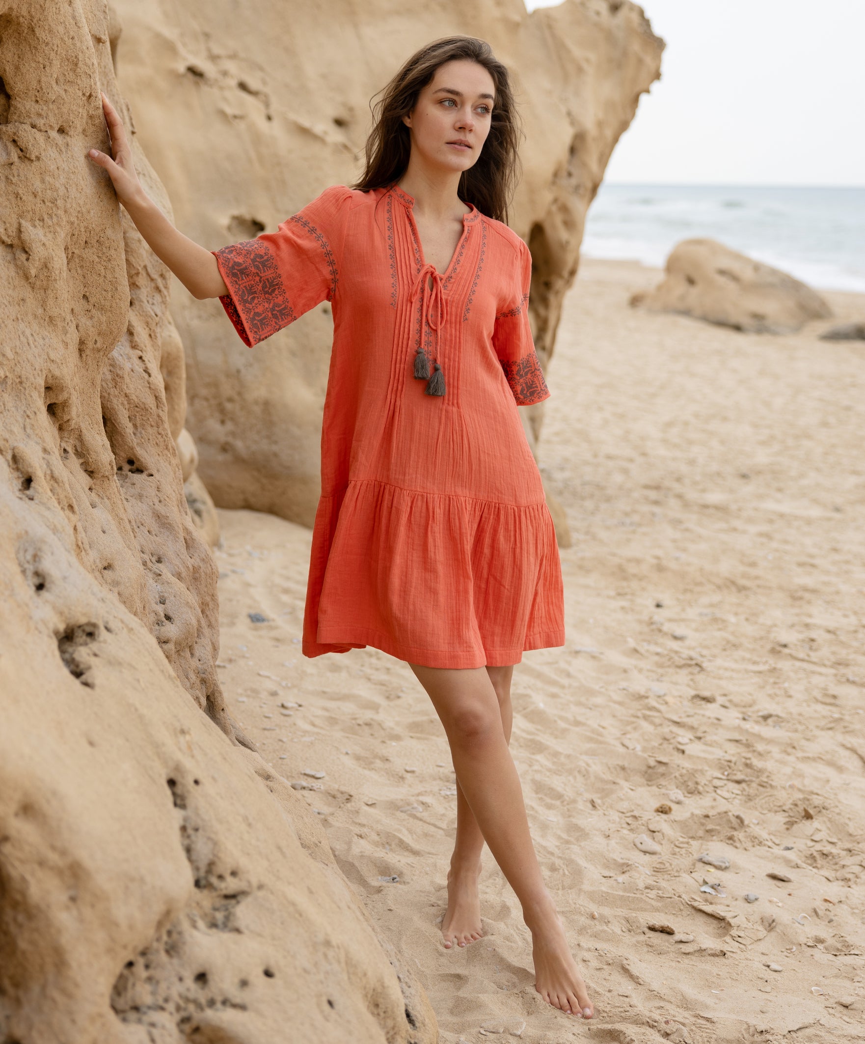A model wears a Rose and Rose embroidered Ajaccio dress in coral cotton.