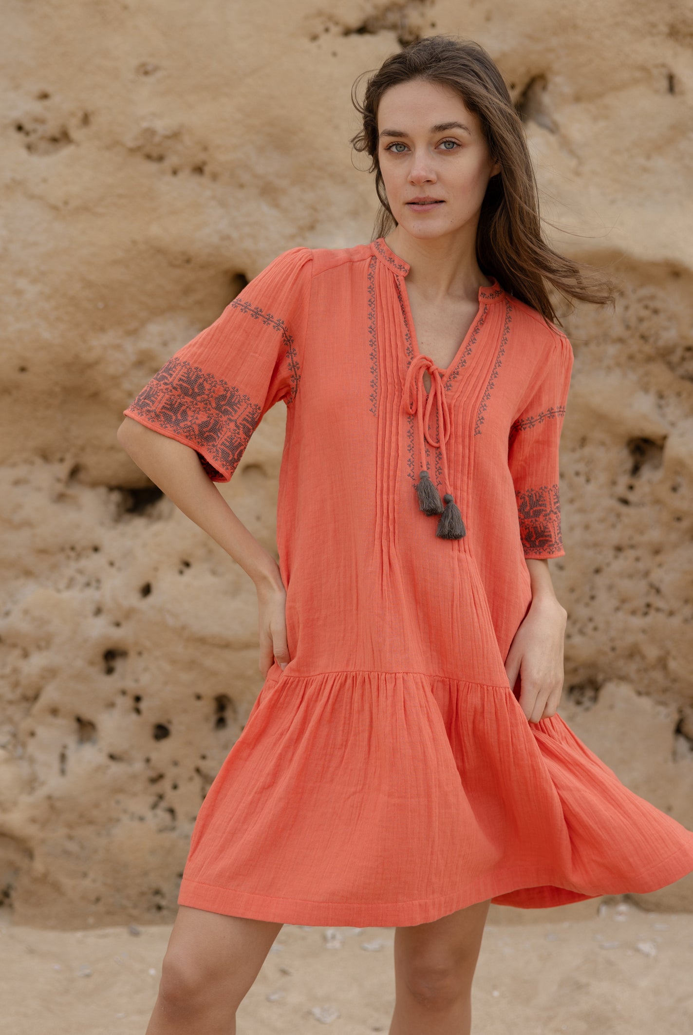 A model wears a Rose and Rose embroidered Ajaccio dress in coral cotton.