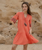 A model wears a Rose and Rose embroidered Ajaccio dress in coral cotton.