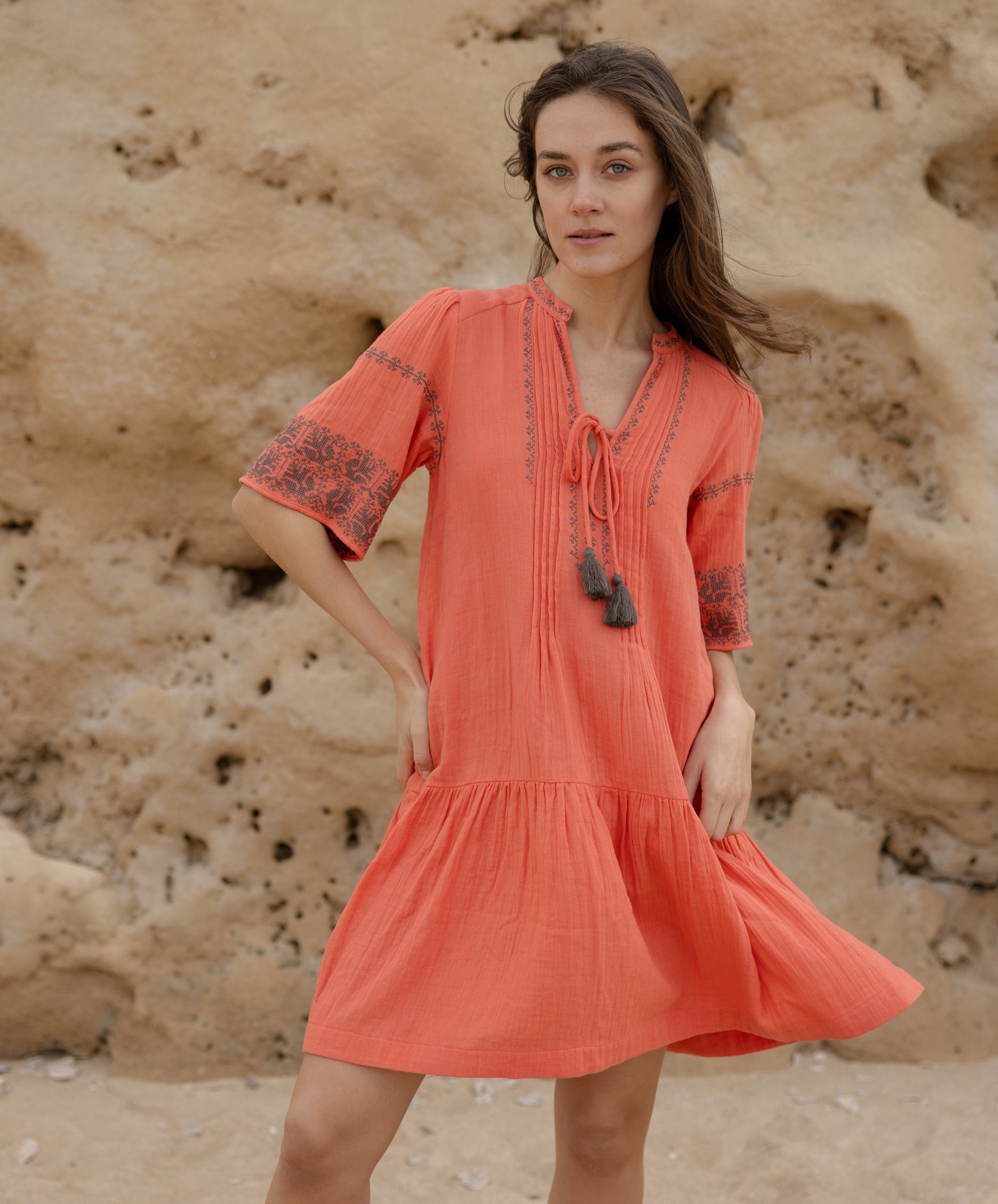 A model wears a Rose and Rose embroidered Ajaccio dress in coral cotton.