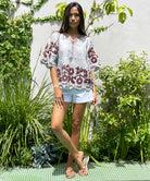 A model stood in a garden wearing a Rose and Rose striped linen Alassio top with white shorts.