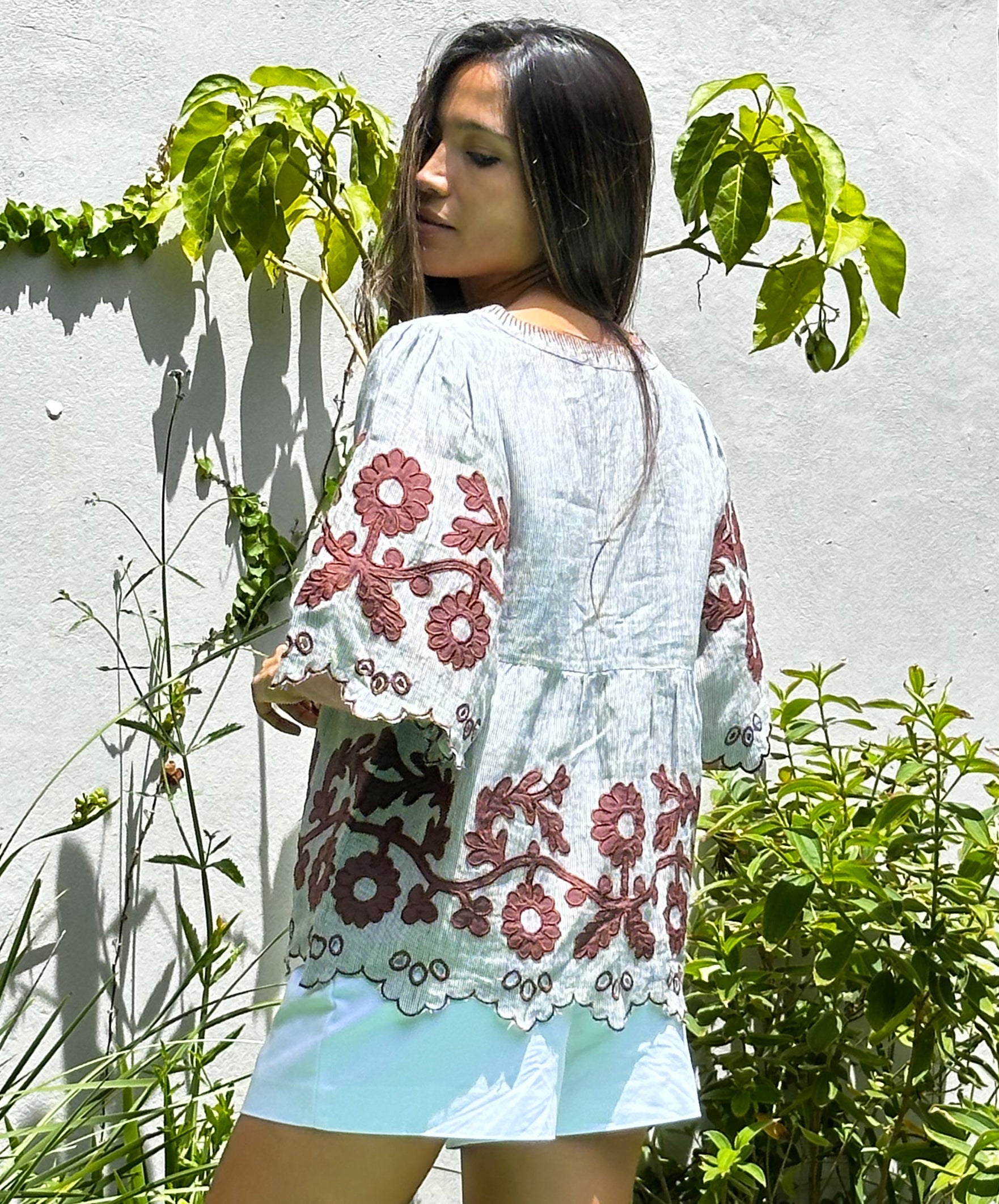 Back view of a model wearing a Rose and Rose striped linen Alassio top with white shorts.