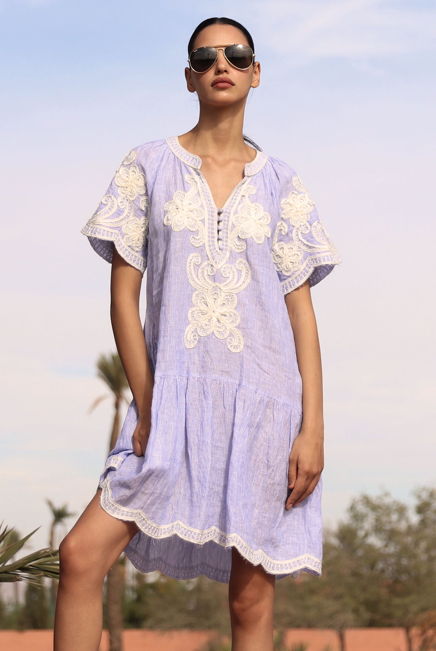 Woman wearing a striped blue Amaranta dress with white tape decoration with sunglasses against a desert background