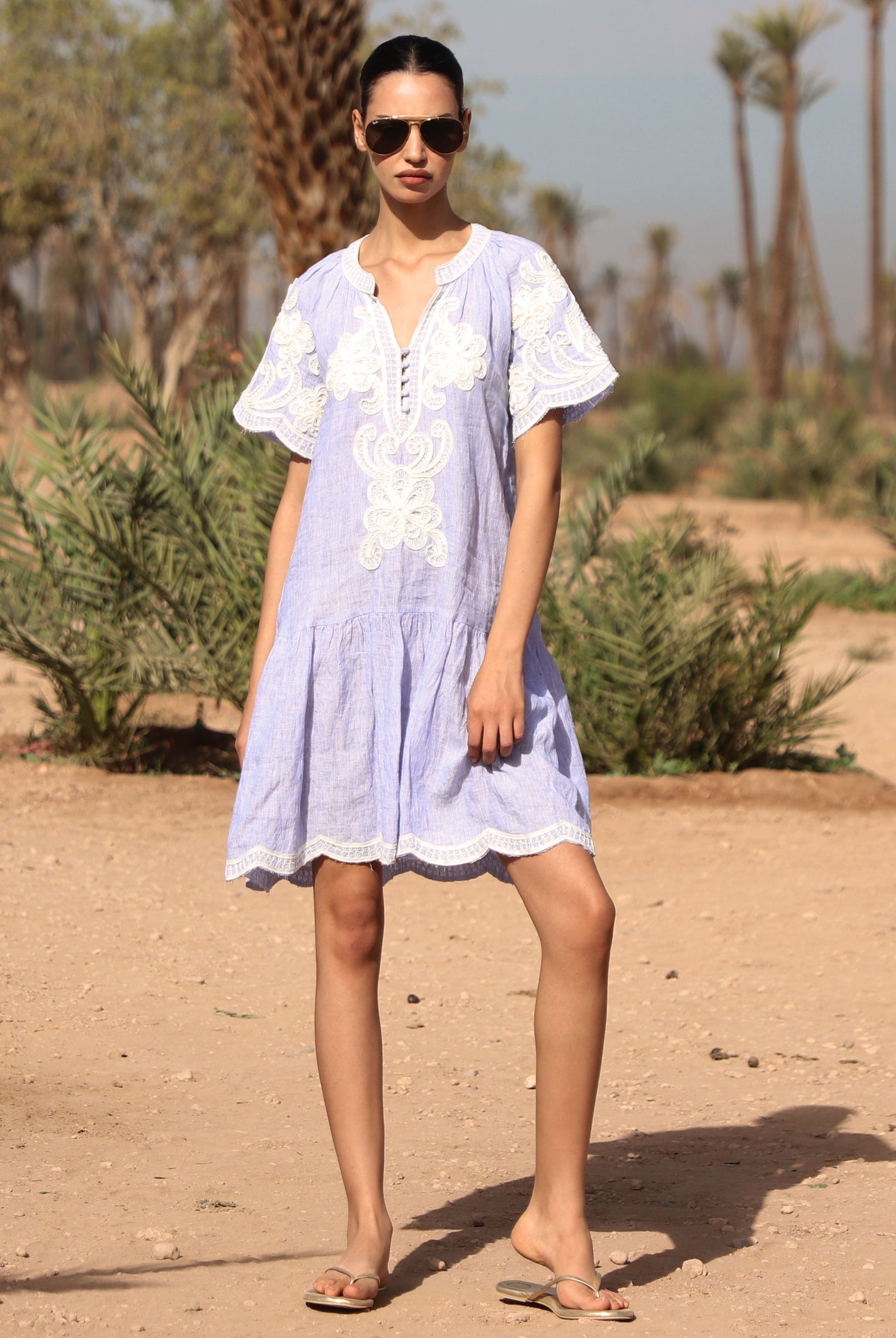 Woman in a striped blue Amaranta dress with white tape decoration standing in a desert-like setting.