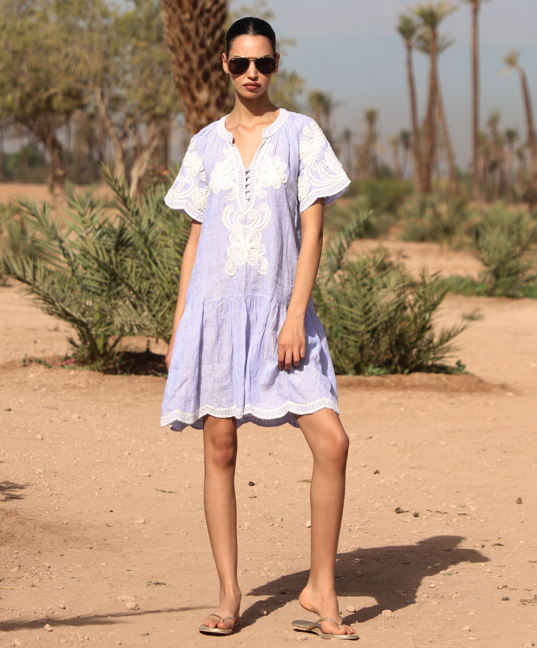 Woman in a striped blue Amaranta dress with white tape decoration standing in a desert-like setting.