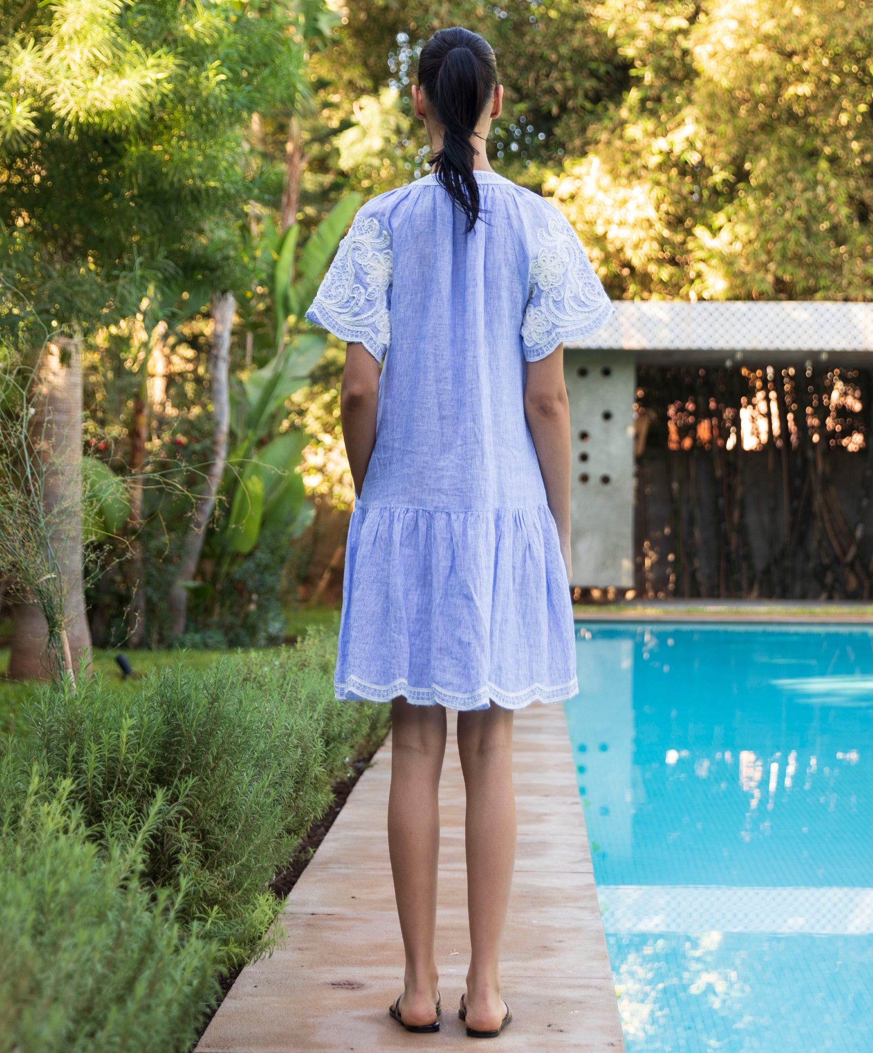 Back view of a woman in a striped blue Amaranta dress standing by a pool.
