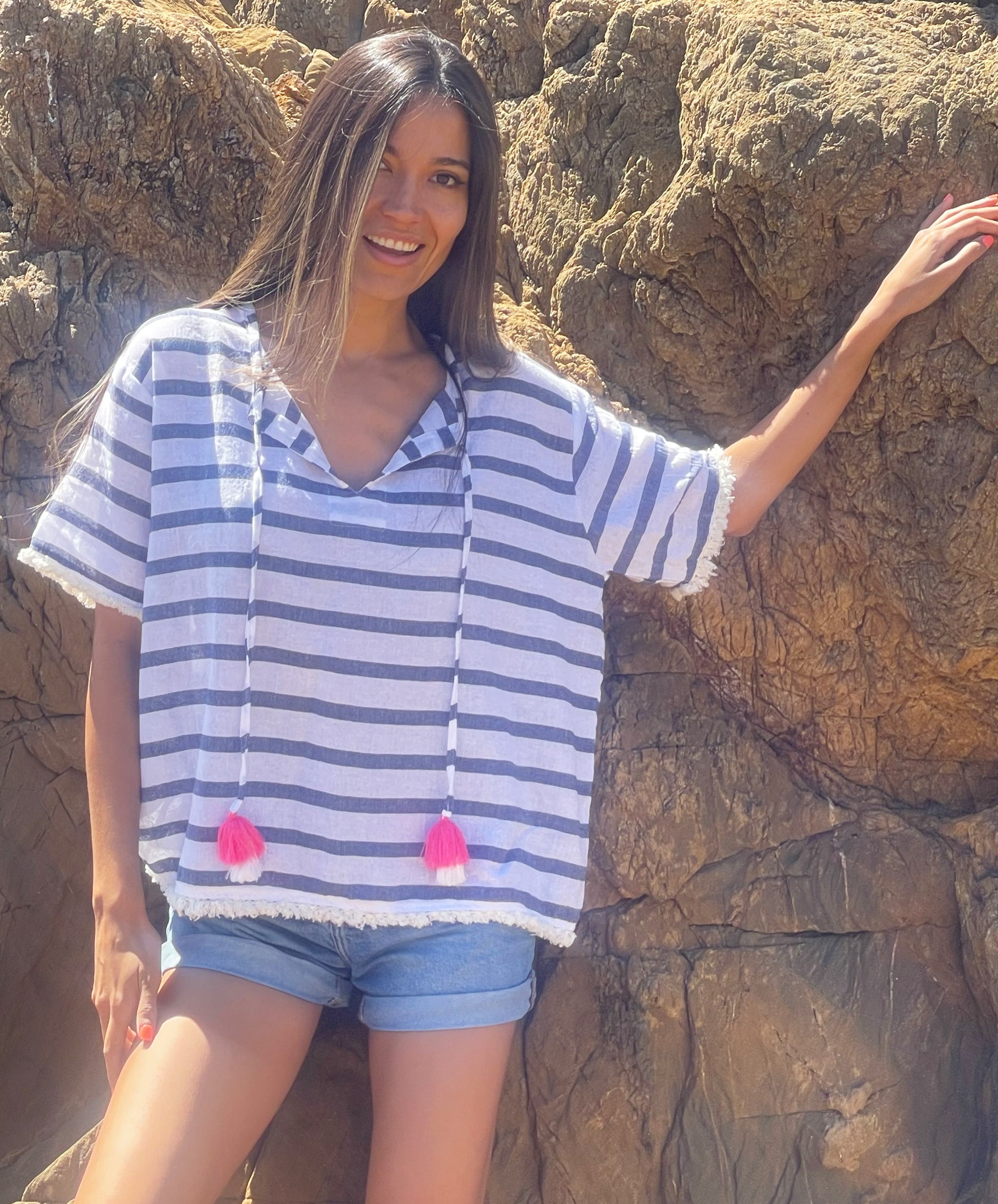 A close up of a model in front of rocks wearing a Rosebud by Rose and Rose Antibes top and denim cut off shorts. 