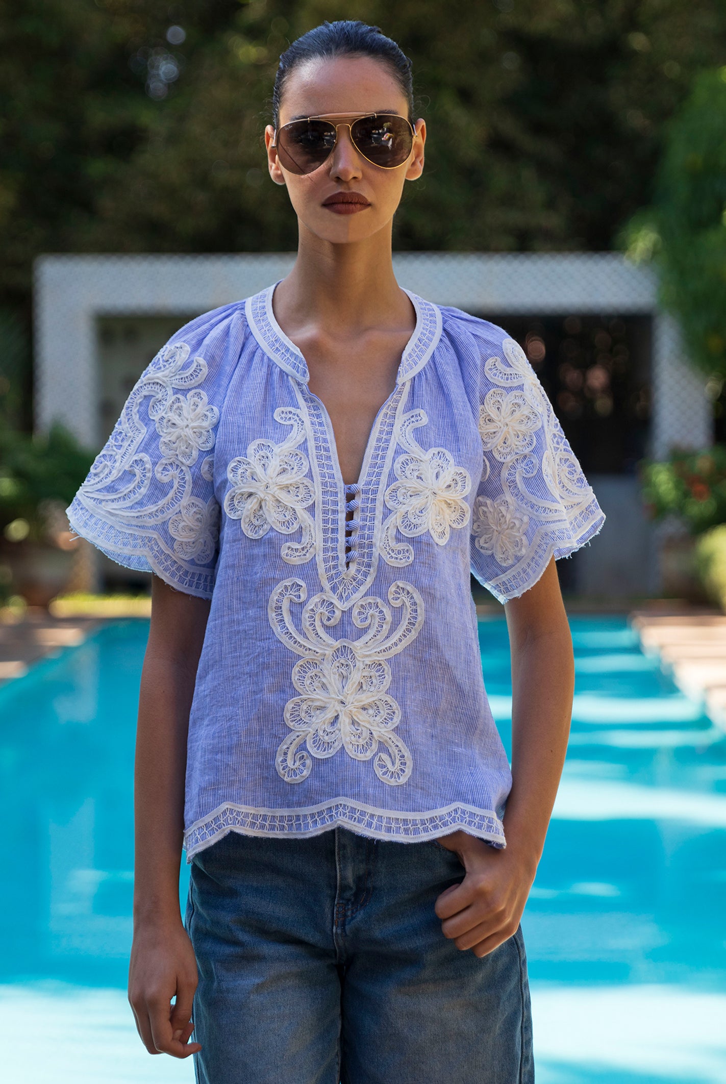 Woman wearing a blue striped embroidered Azalea top by a pool