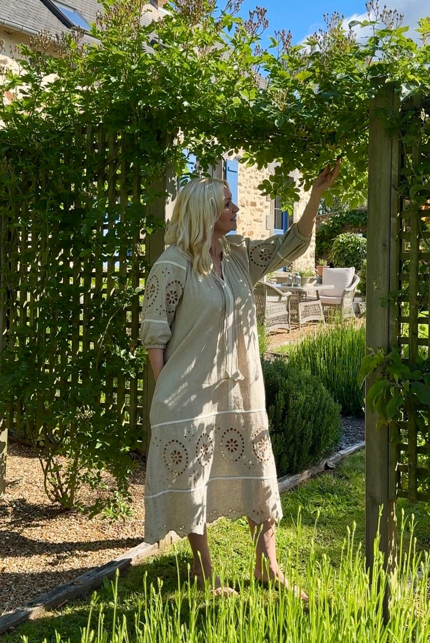Influencer @shutters_and_stone stood admiring her garden wearing the Magnolia natural embroidered dress
