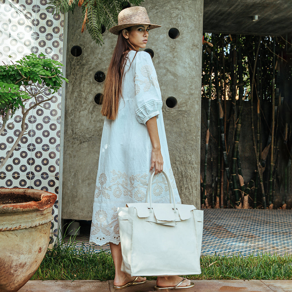 A model wearing a Rose and Rose Grange dress in White with sand appliqué decoration, a summer cotton canvas bag and a straw hat.