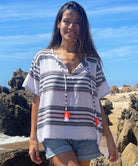 A close up of a model on a beach wearing a Rosebud by Rose and Rose top with denim cut off shorts. 
