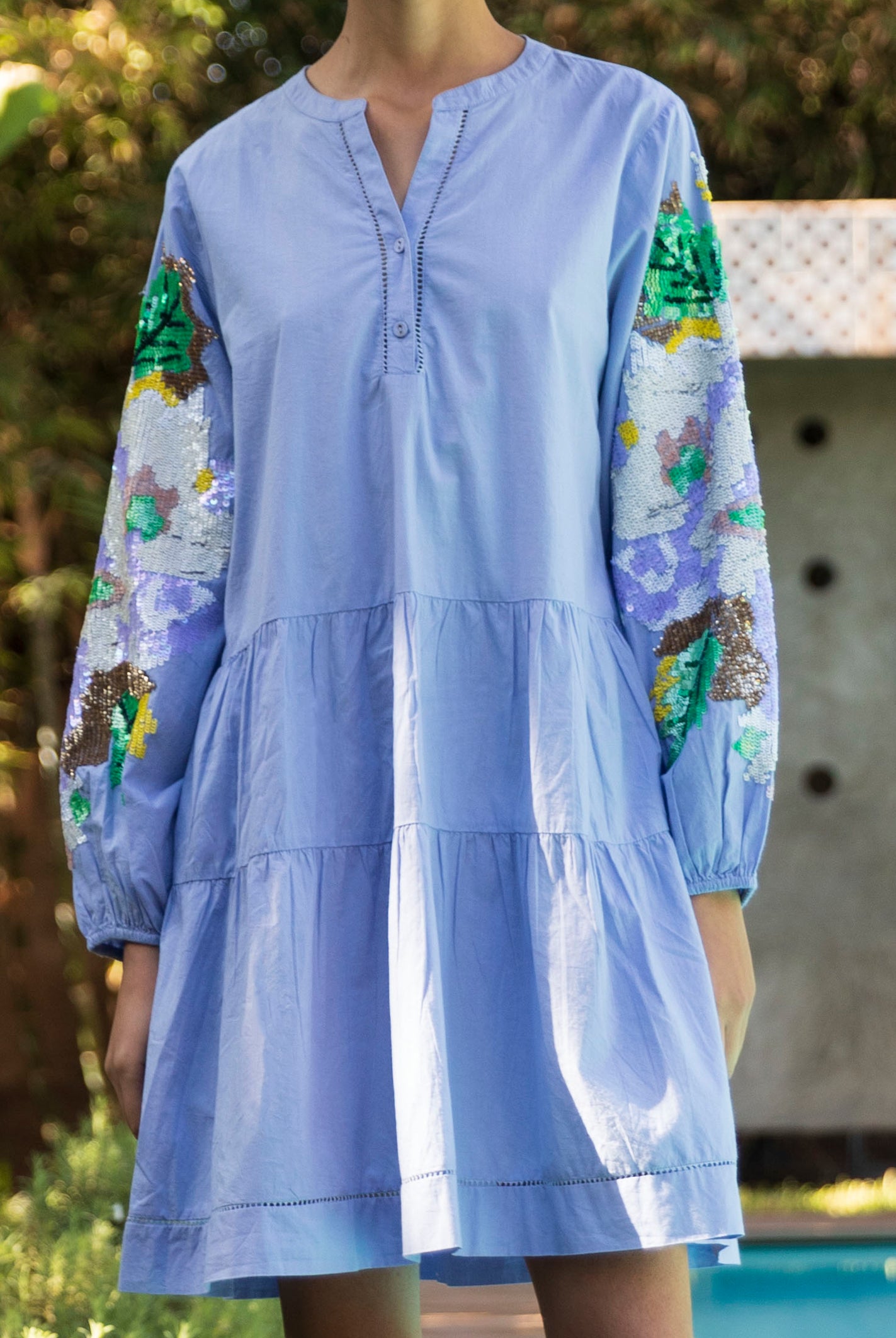 Light blue Beech dress with sequins in floral patterns on sleeves, worn in garden.