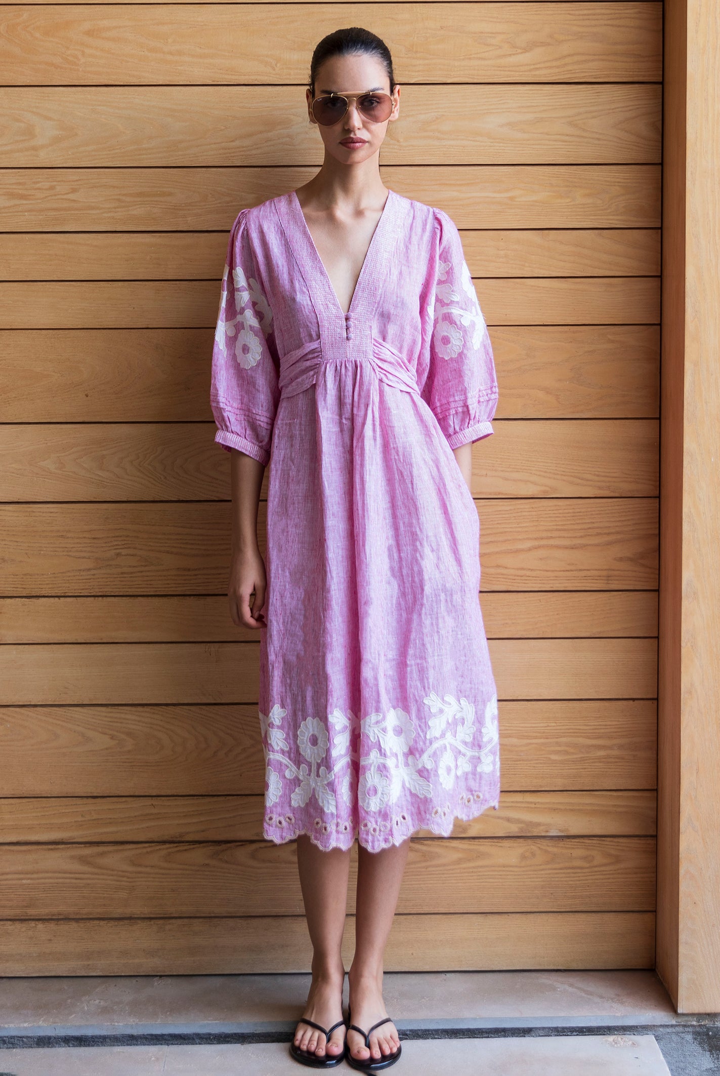 Woman wearing a red striped Begonia dress with floral applique decoration against a wooden wall.