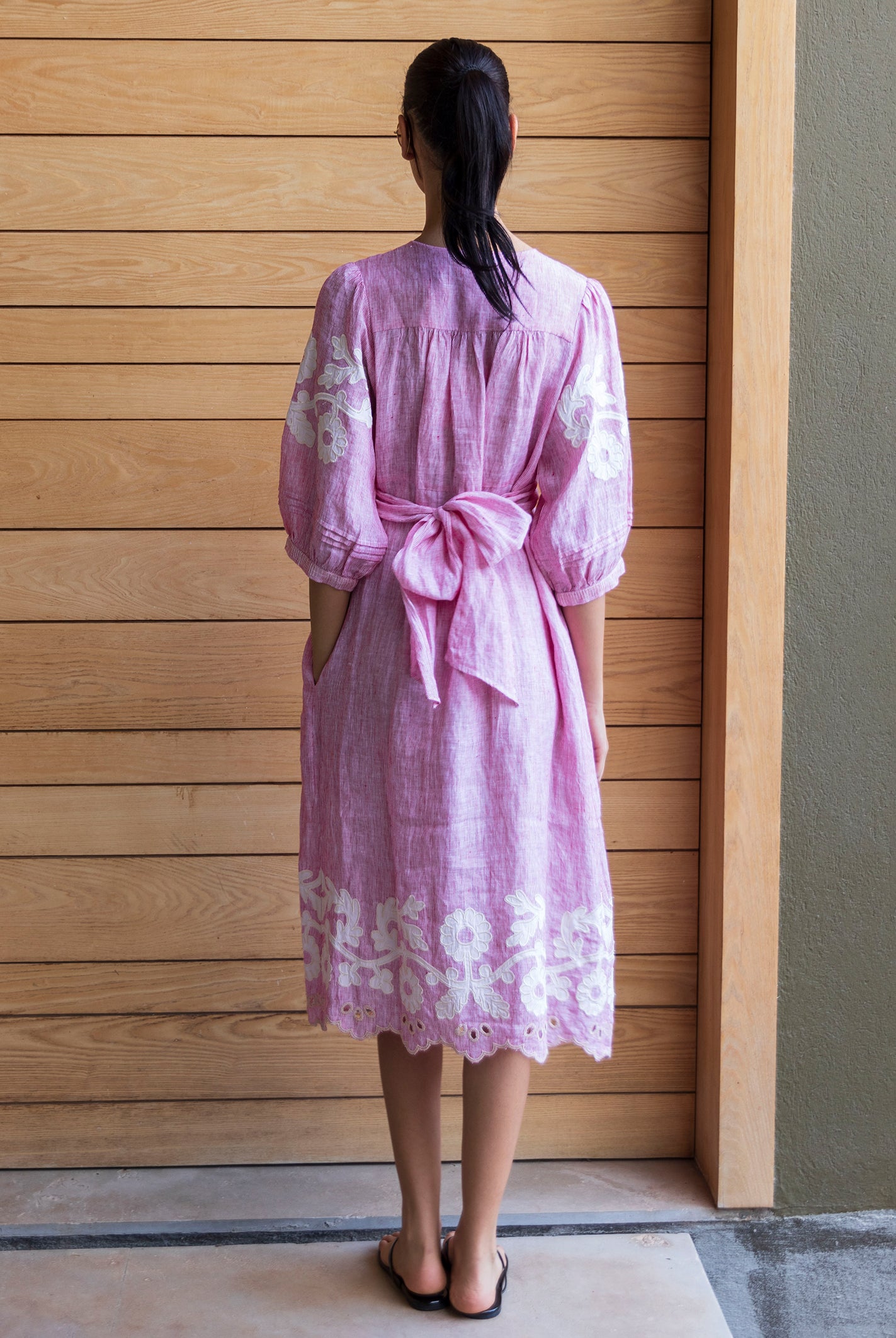 Back view of a woman wearing a red striped Begonia dress with floral applique decoration standing against a wooden door.