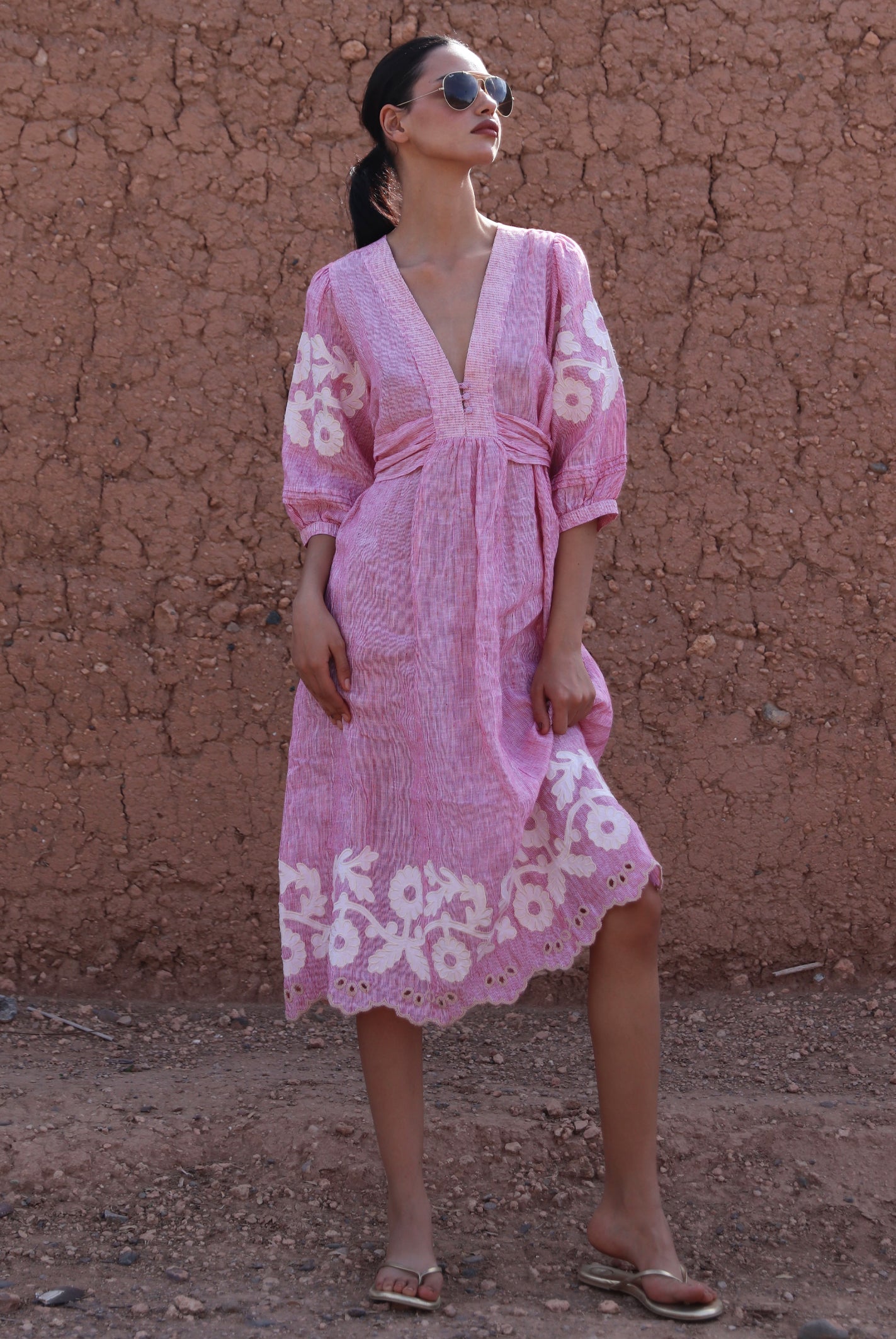Woman wearing a red striped Begonia dress with floral applique decoration against a clay wall.