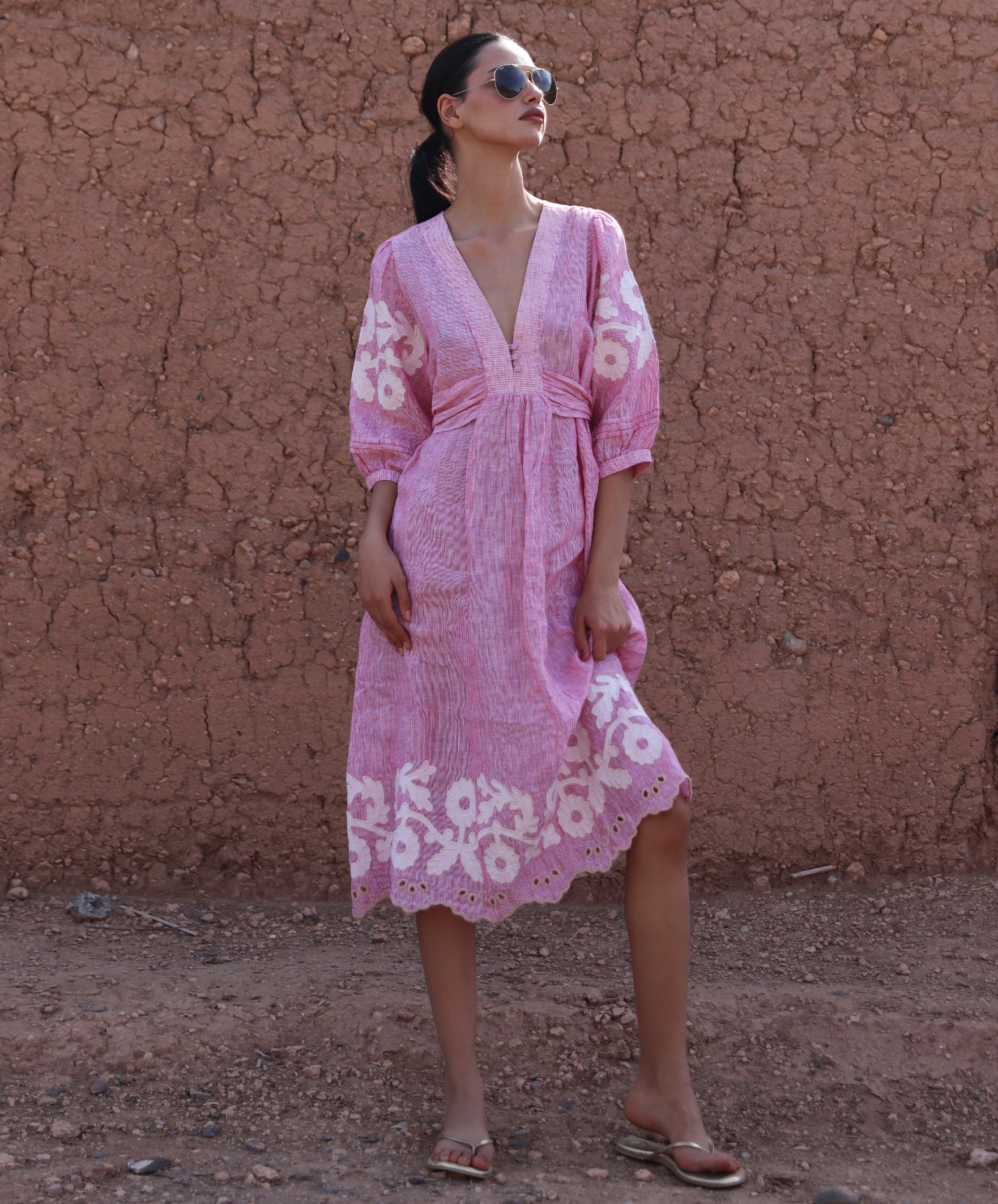 Woman wearing a red striped Begonia dress with floral applique decoration against a clay wall.