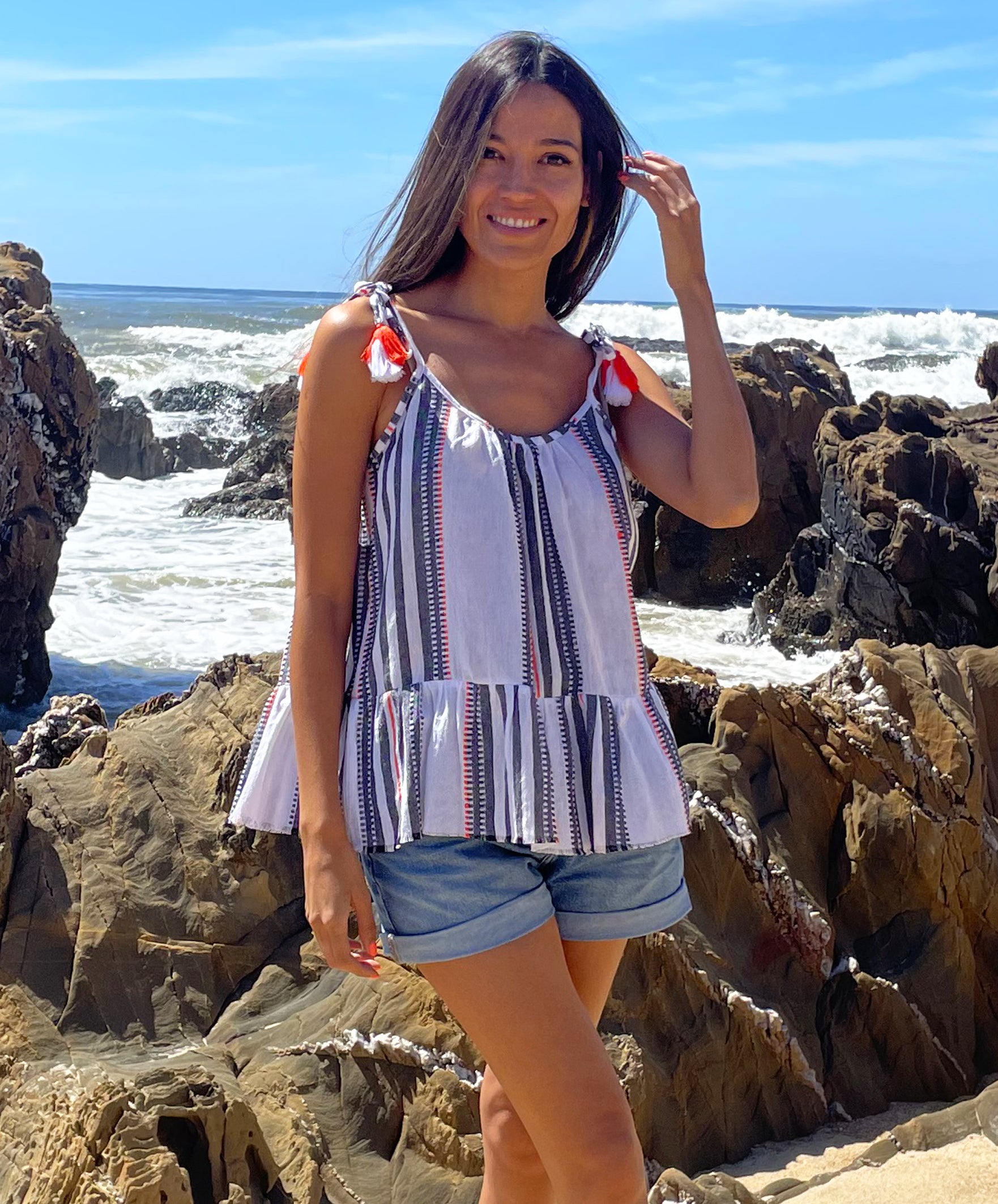 A close up of a model on a beach wearing a Rosebud by Rose and Rose Bergerac Top and denim cut off shorts. 