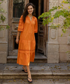 A model wears a Rose and Rose embroidered Biarritz dress in saffron orange cotton.