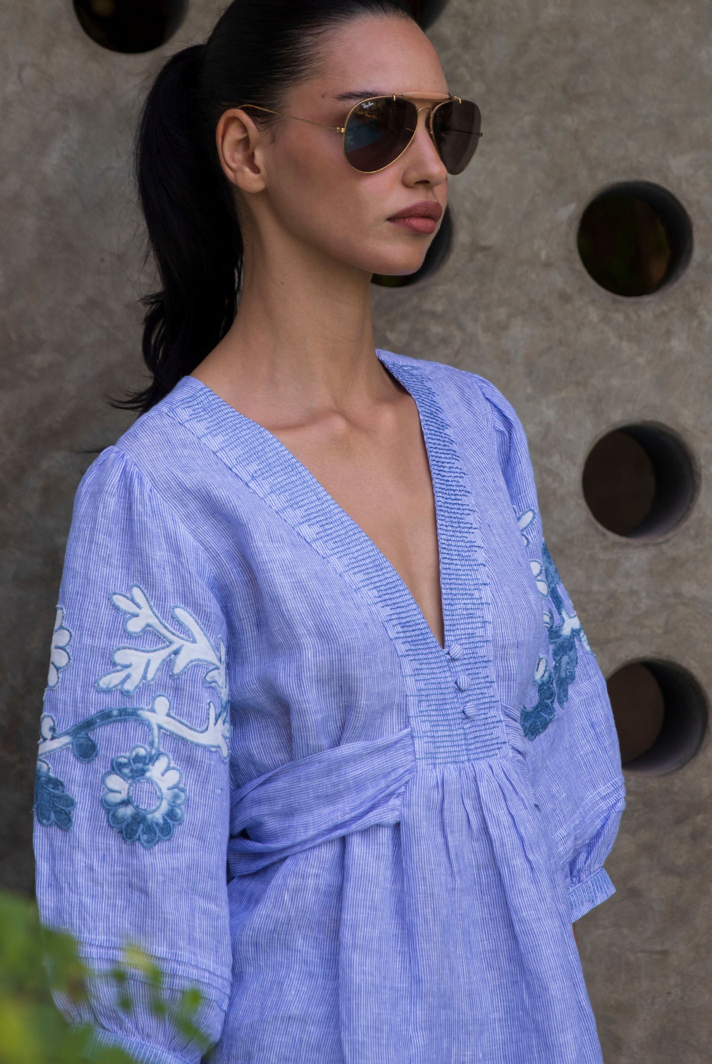 Woman wearing blue striped embroidered Blossom blouse against a textured wall.