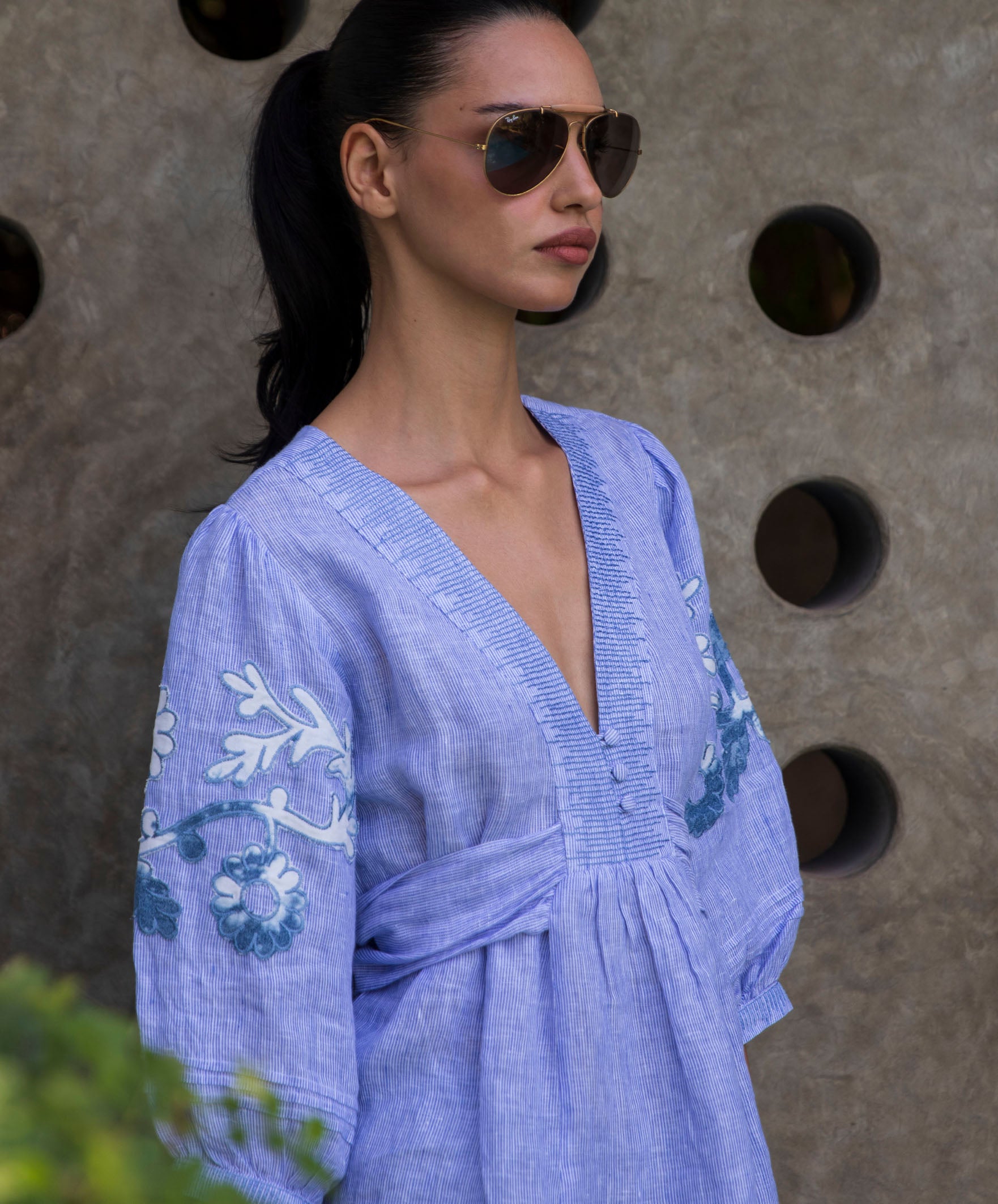 Woman wearing blue striped embroidered Blossom blouse against a textured wall.