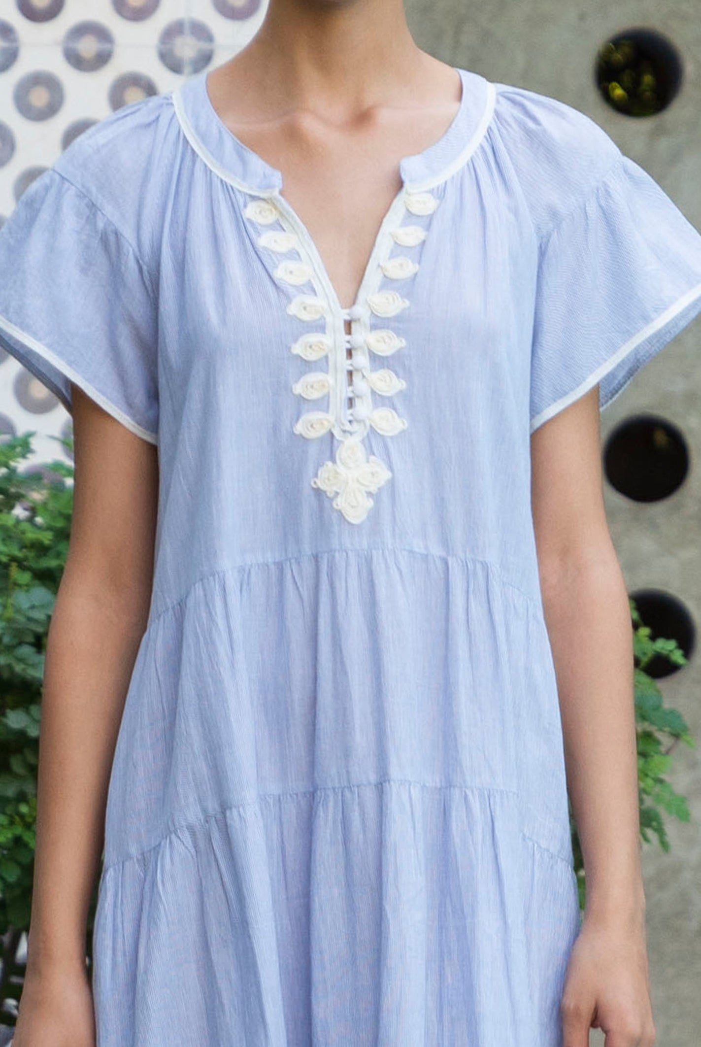 Striped blue Camelia dress with white passementerie embroidery details worn by a woman