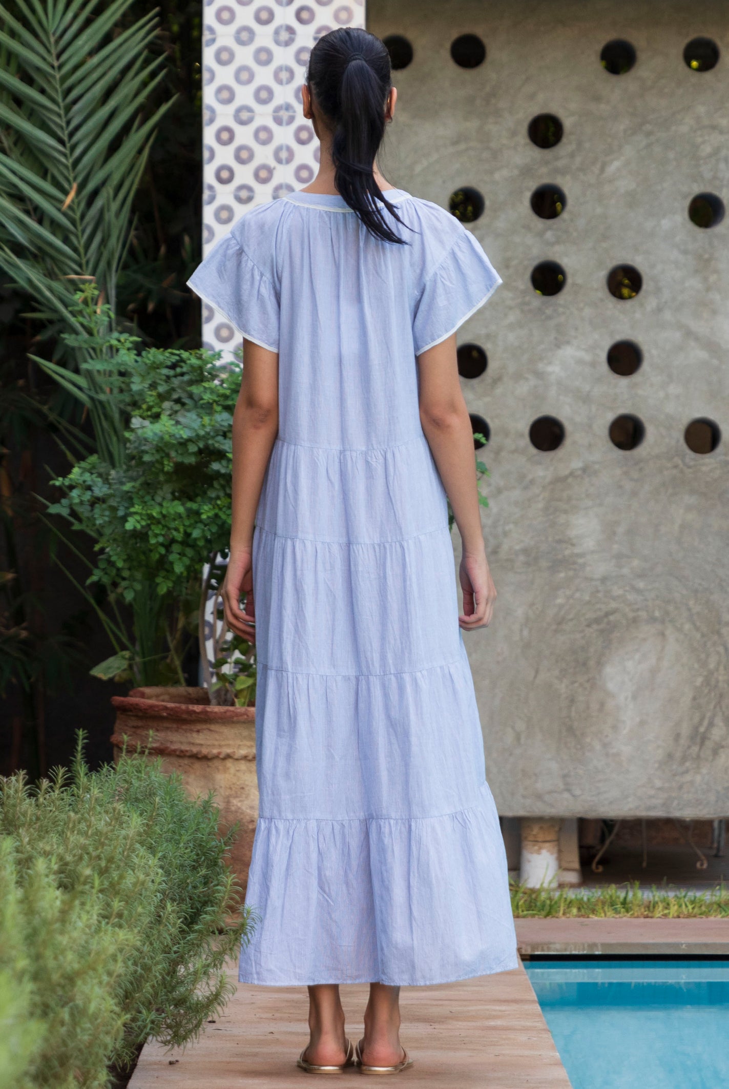 Back view of woman in a blue striped Camelia dress standing by a pool
