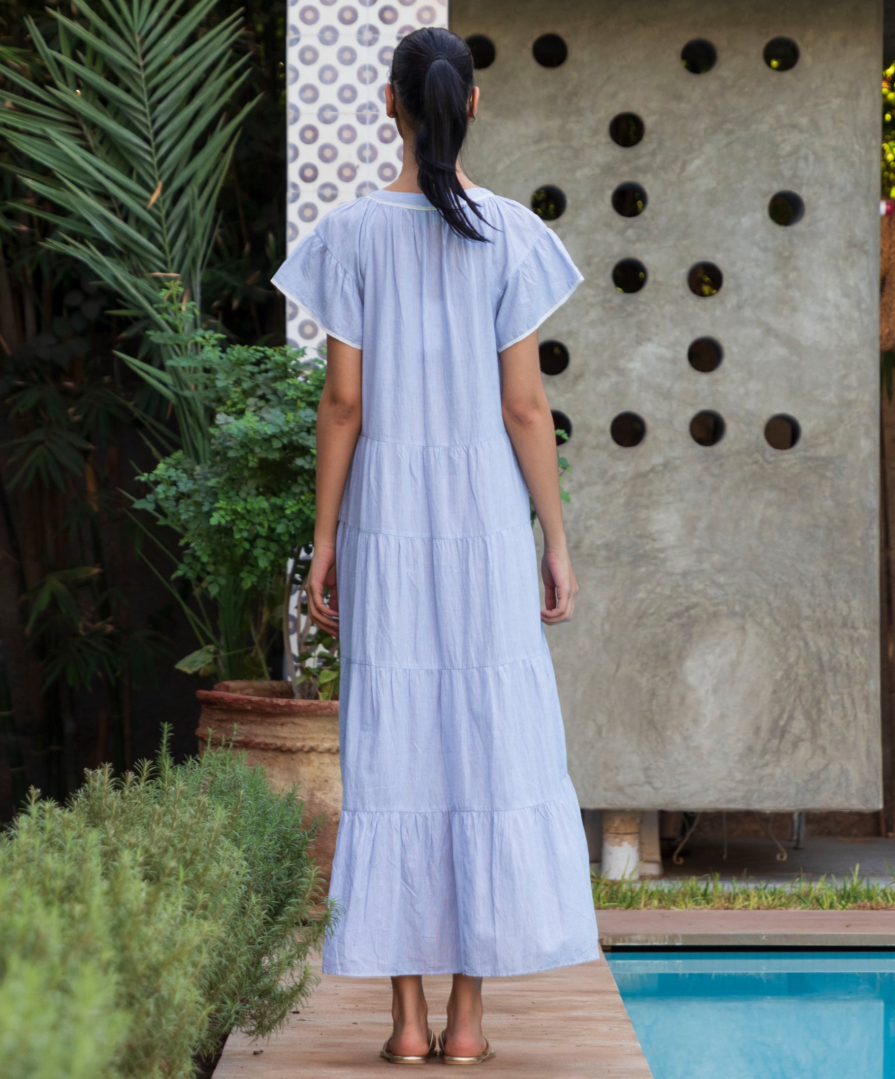 Back view of woman in a blue striped Camelia dress standing by a pool