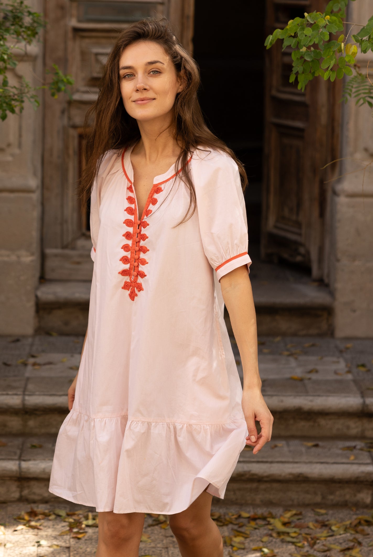 A model wearing a Rose and Rose pink cotton Cannes dress with passementerie decoration.