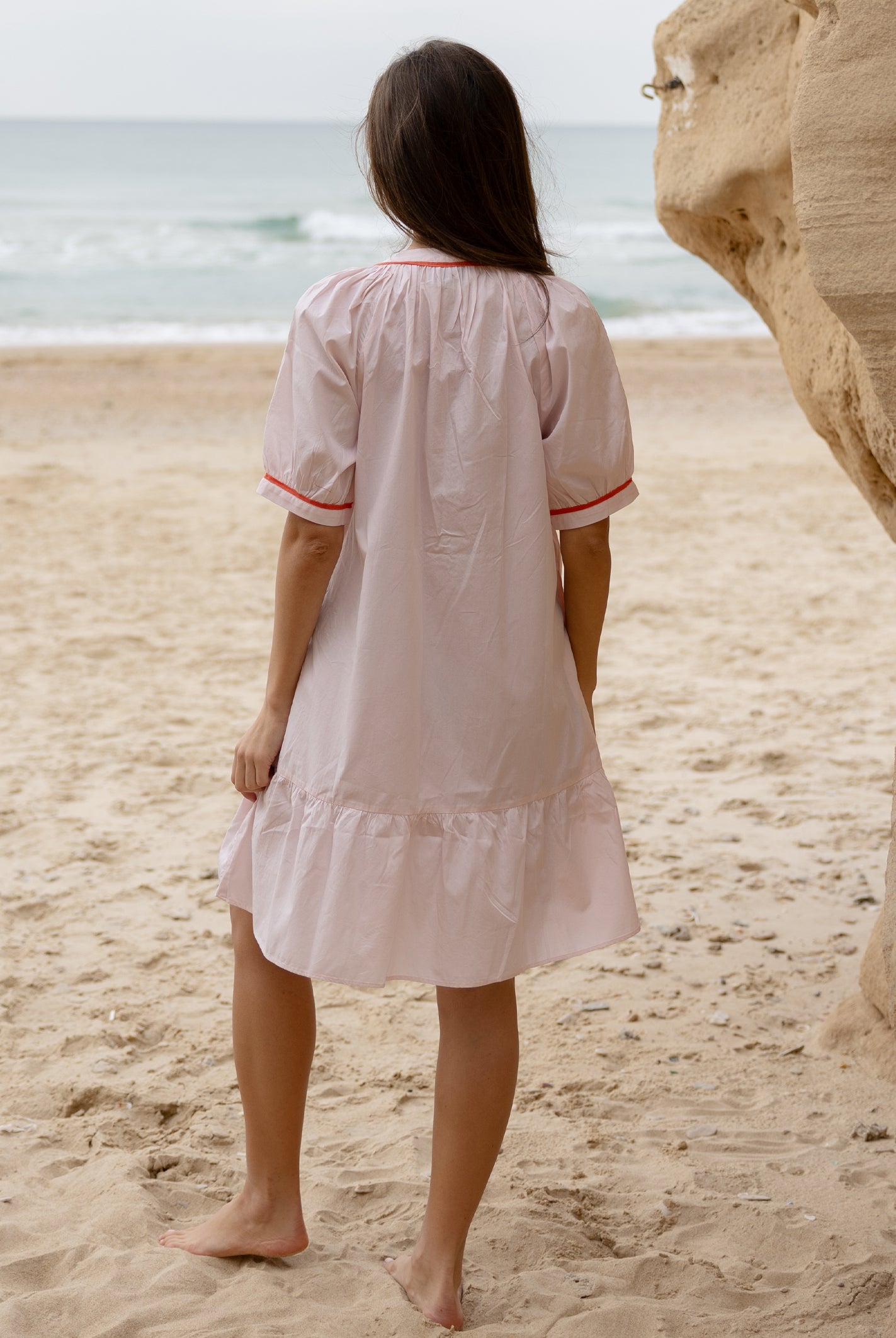 Back view of a model wearing a Rose and Rose pink cotton Cannes dress with passementerie decoration.