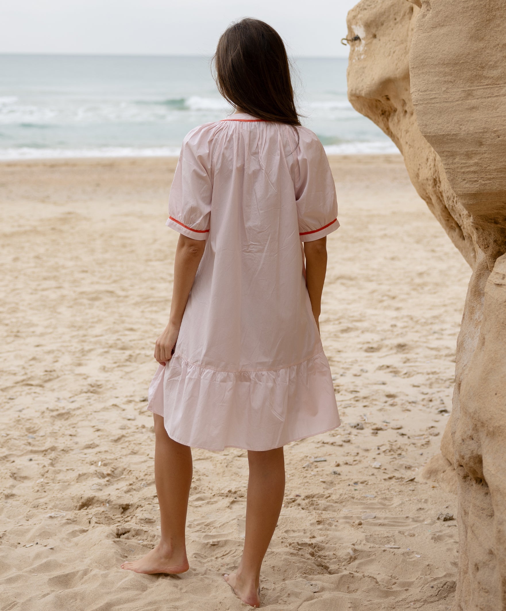 Back view of a model wearing a Rose and Rose pink cotton Cannes dress with passementerie decoration.