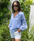 A model stood in a garden wearing a Rose and Rose blue cotton Capri top, white shorts and sunglasses.  