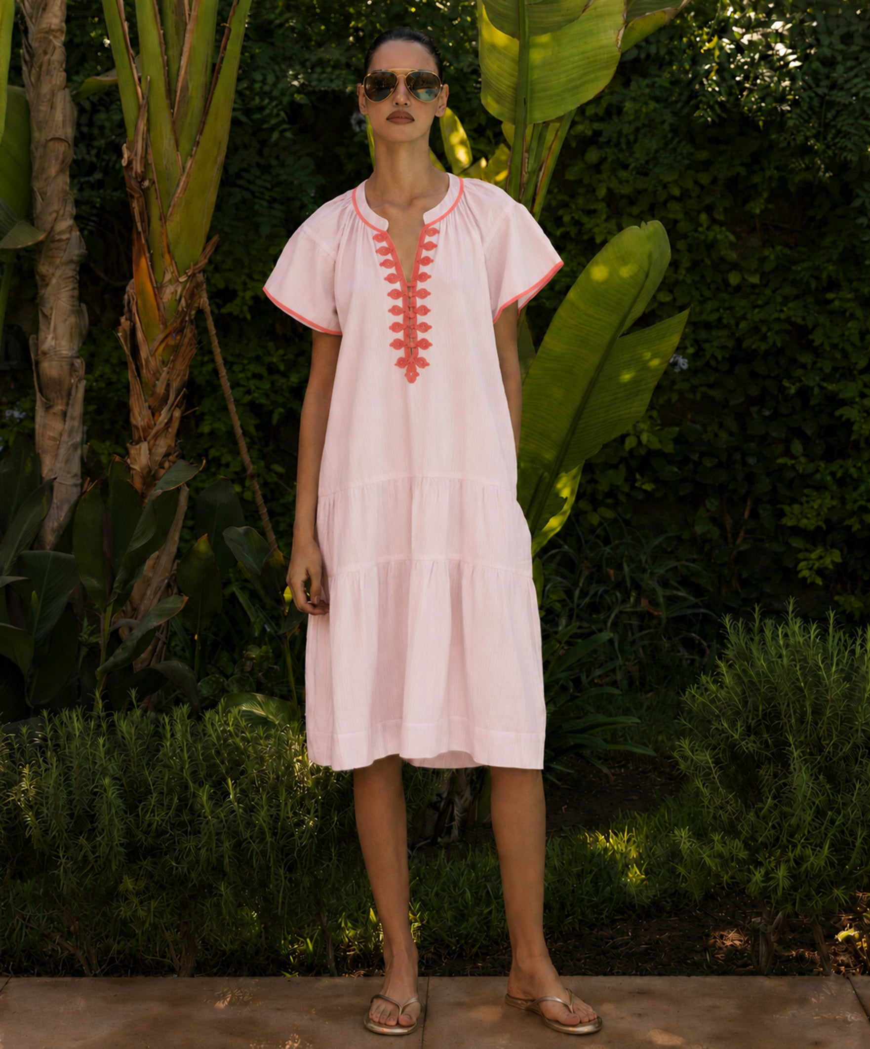 Woman wearing a light pink dress with red embroidery in a tropical garden setting