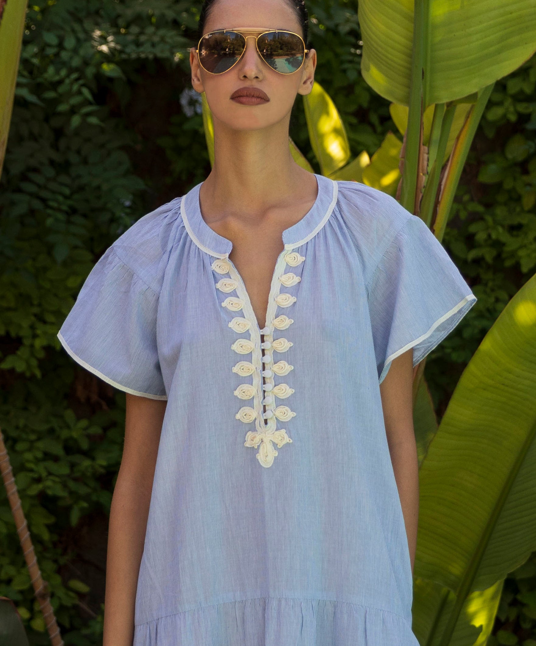 Close up of a model wearing a blue striped dress with white passementerie embroidery.