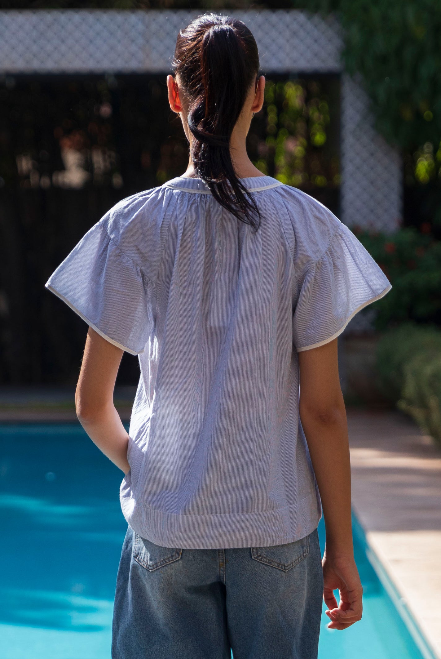 Back view of a woman wearing a blue striped Clematis top by a poolside
