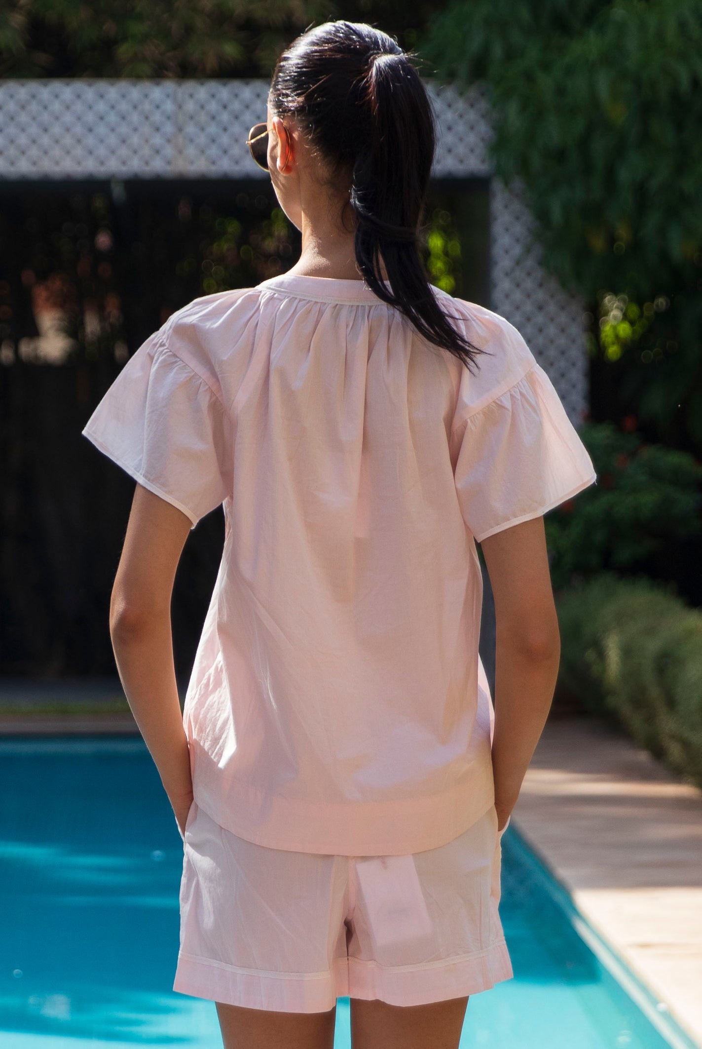 Back view of a women wearing a light pink Clematis top and shorts by a poolside