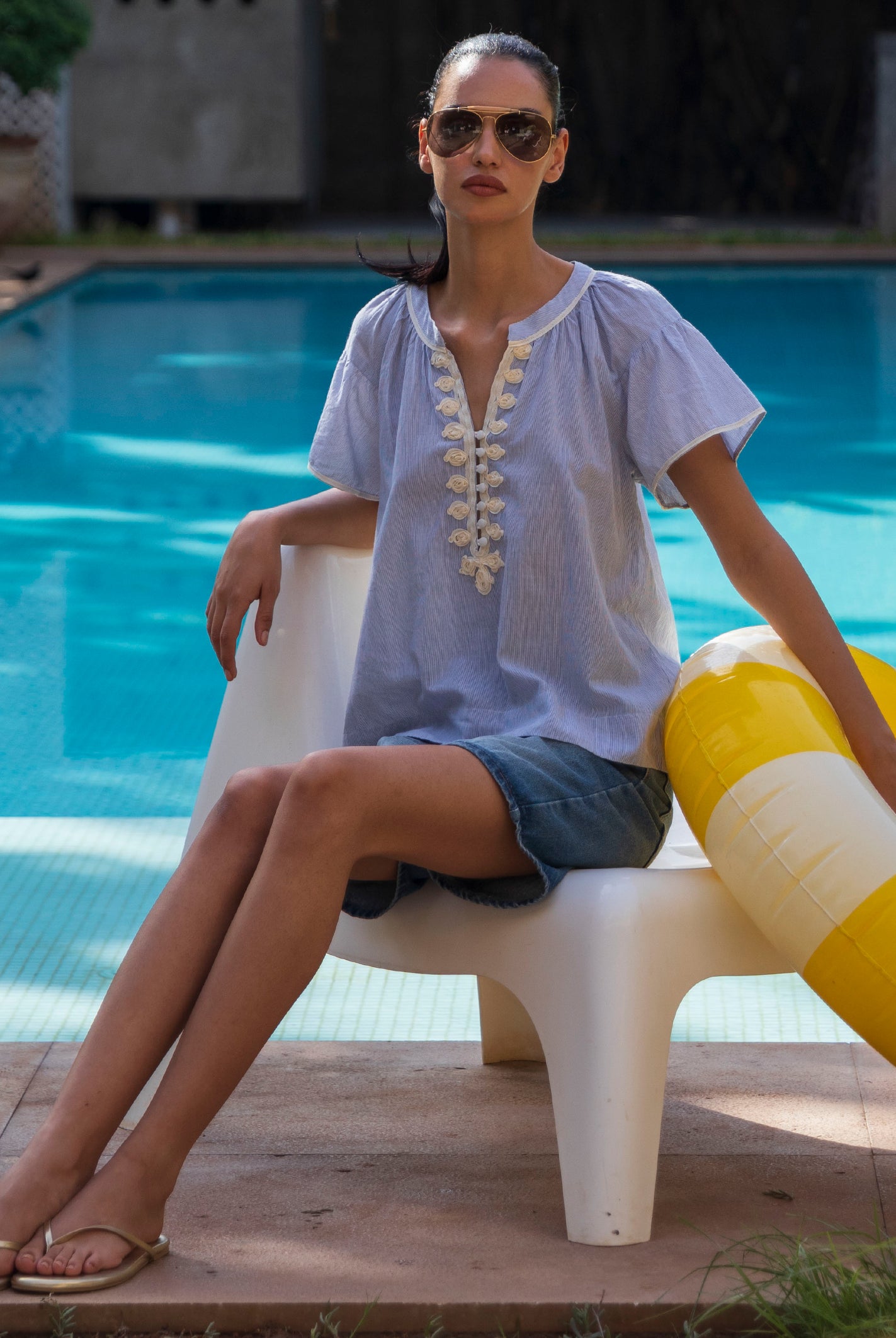 Woman sitting by a pool in a striped Clematis top with a yellow and white inflatable ring