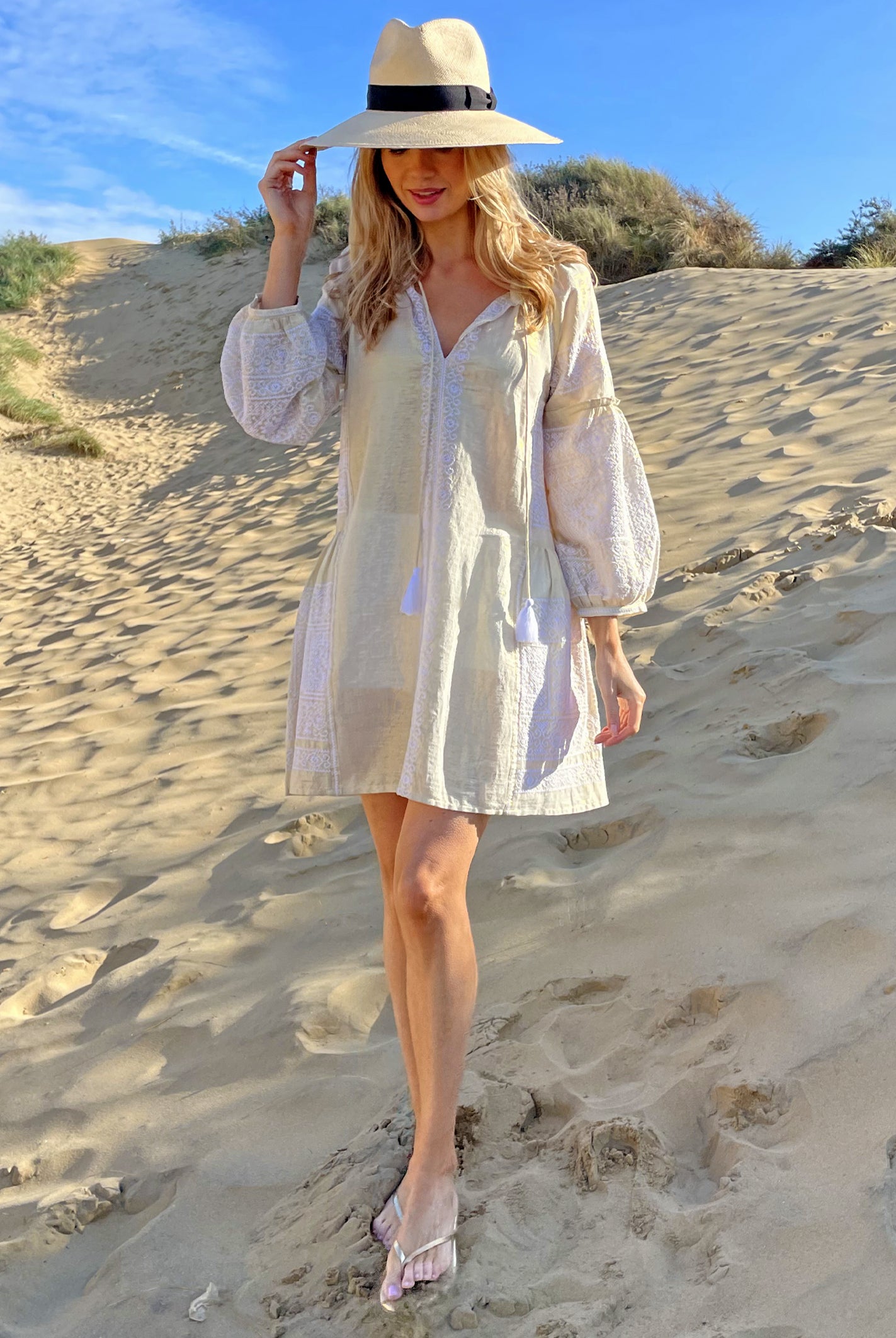 A model on a beach wearing the Rose and Rose Como dress in gold lurex and an Anthony Peto Panama hat.