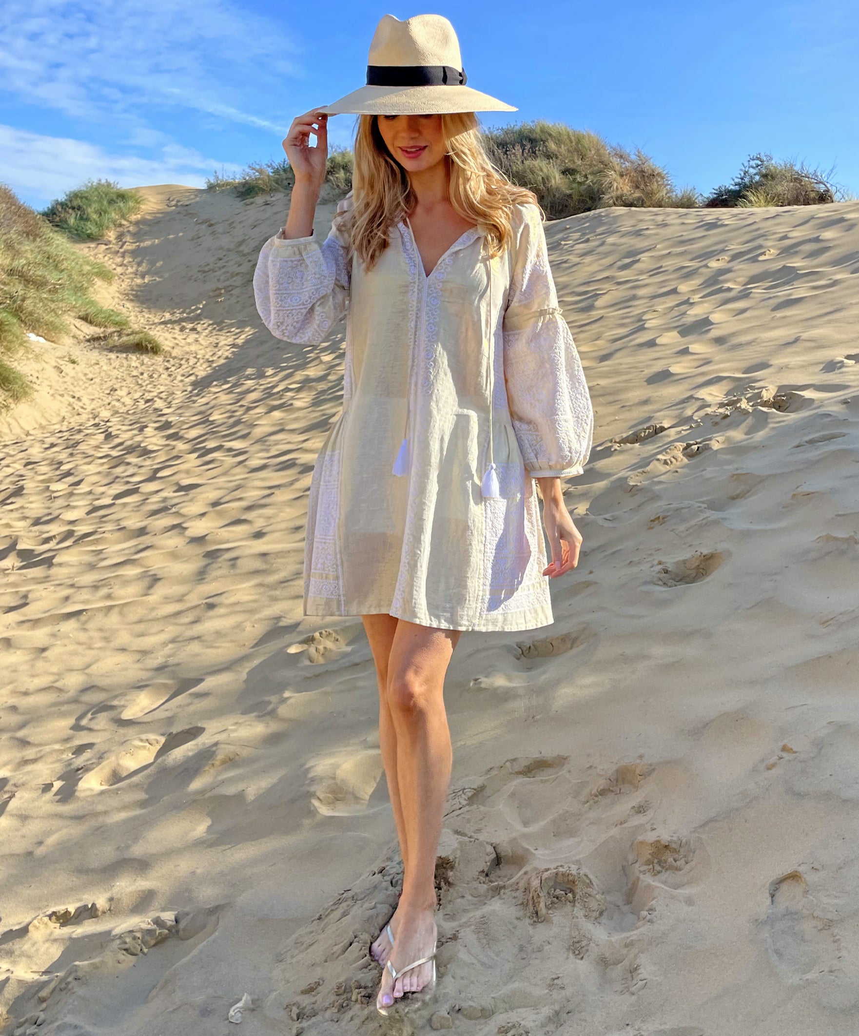 A model on a beach wearing the Rose and Rose Como dress in gold lurex and an Anthony Peto Panama hat.