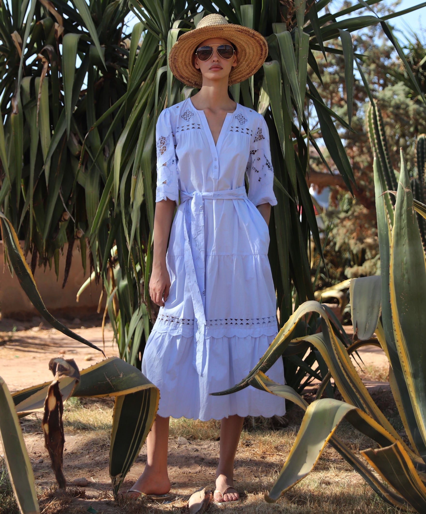 Woman in a light blue Dahlia dress and straw hat standing amongst cacti