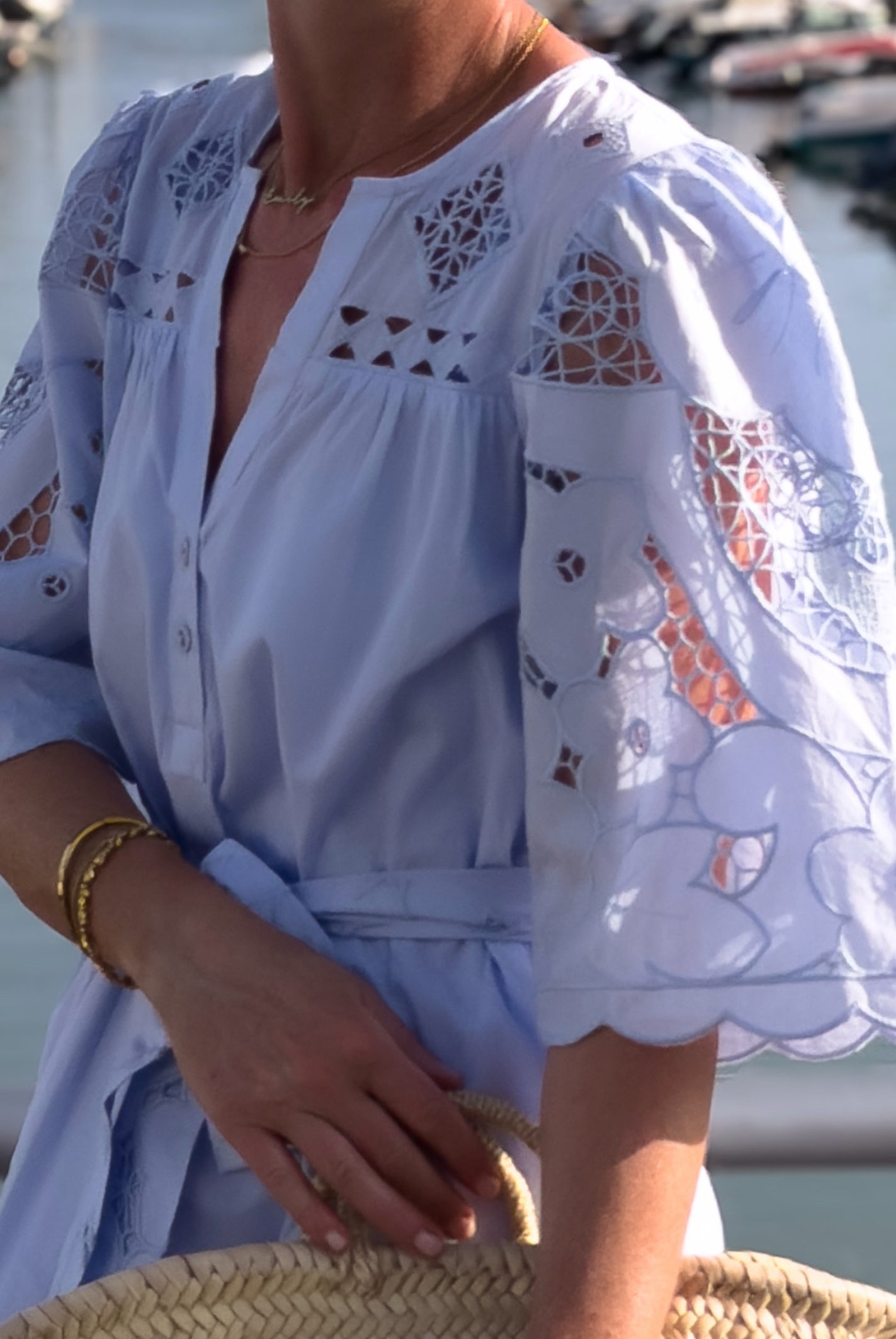 Woman wearing a light blue dress with embroidery details by a waterfront.
