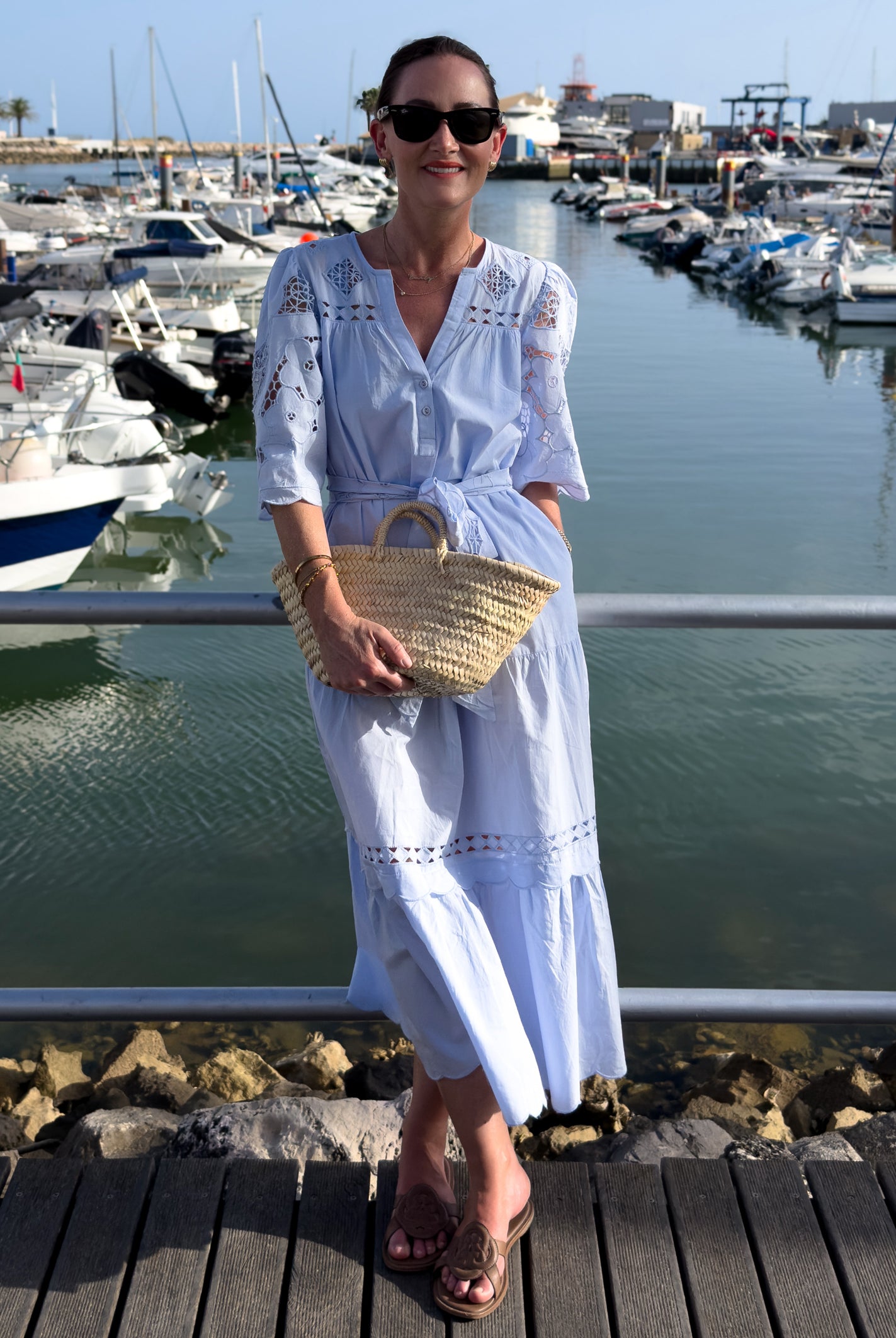 Woman in a light blue dress standing on a dock with boats in the background