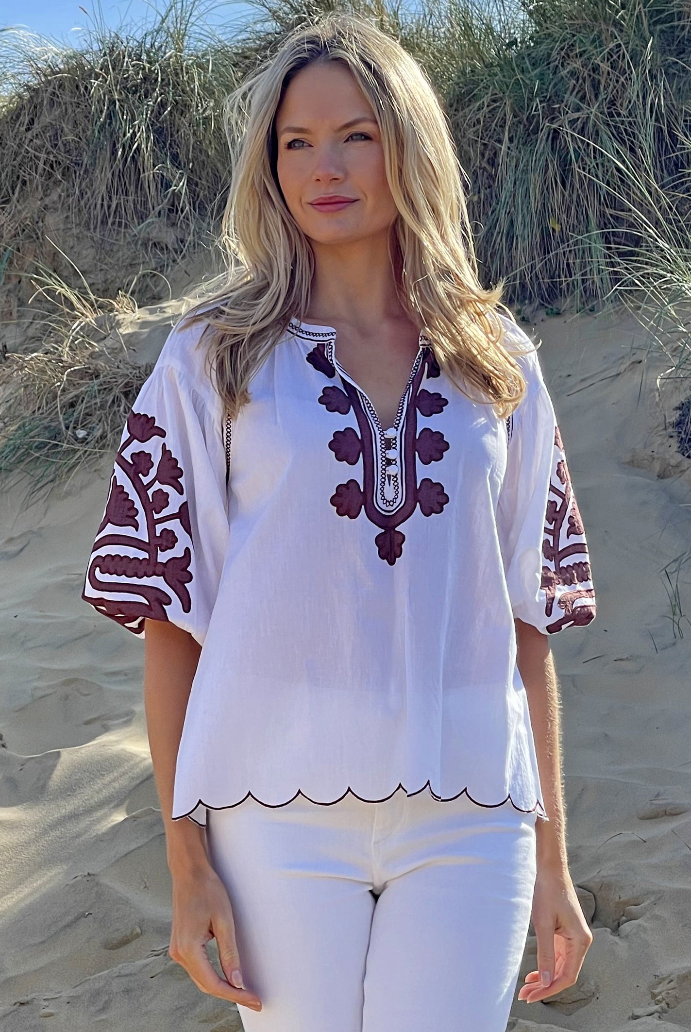 A model on a beach wearing the Rose and Rose Ferrara top in white cotton with bitter chocolate applique.