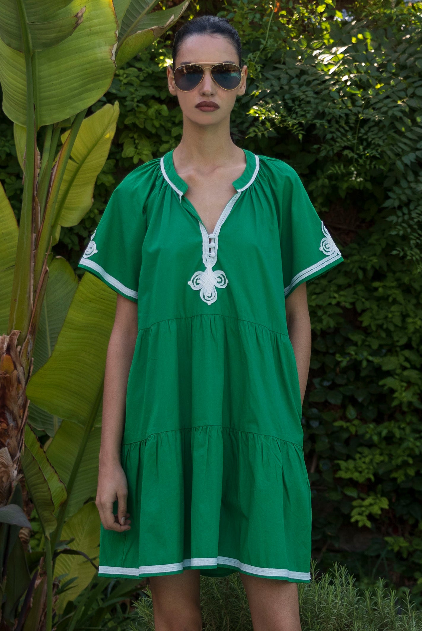 Woman wearing a green Flora dress with white passementerie trim in a tropical garden setting