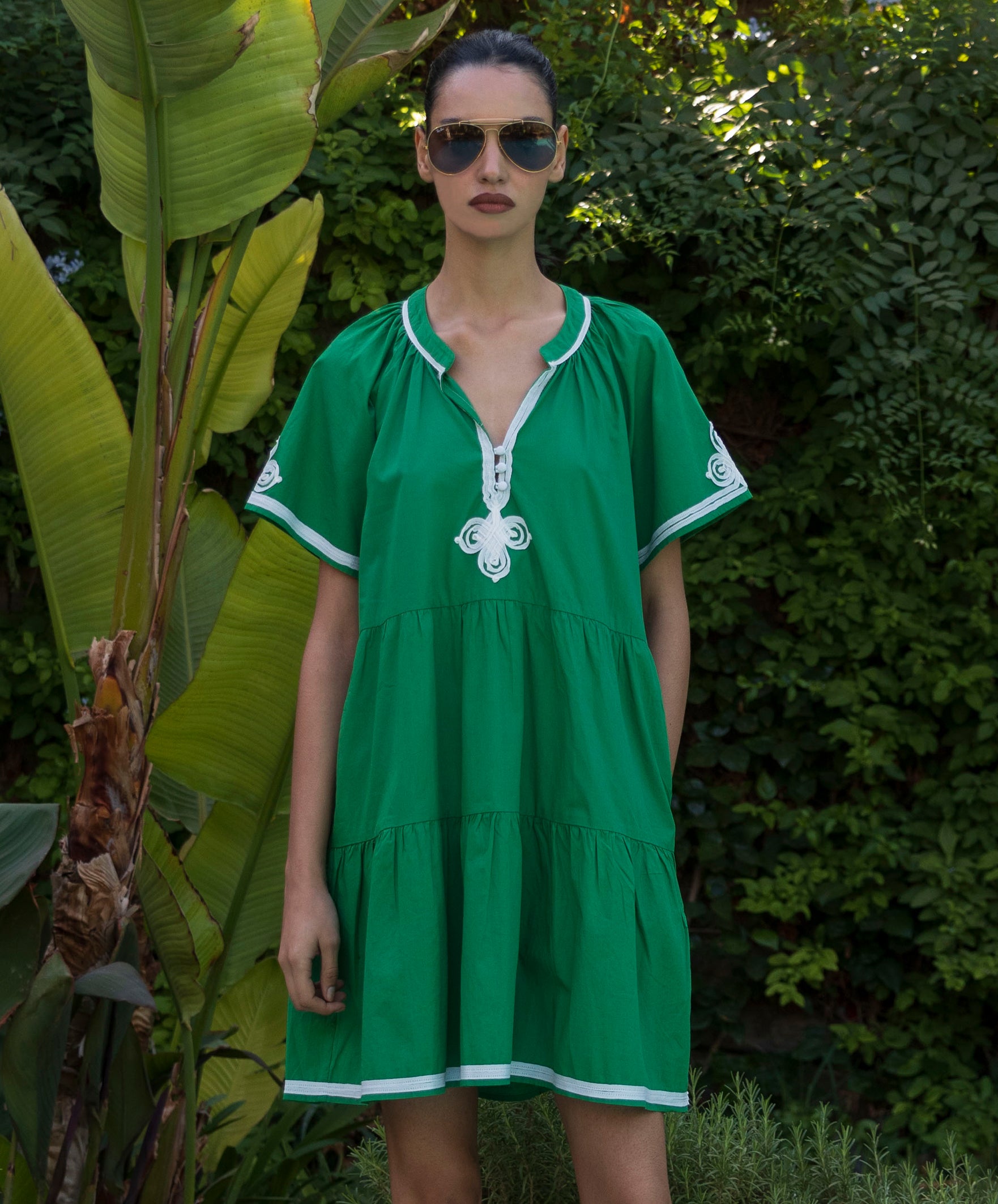 Woman wearing a green Flora dress with white passementerie trim in a tropical garden setting