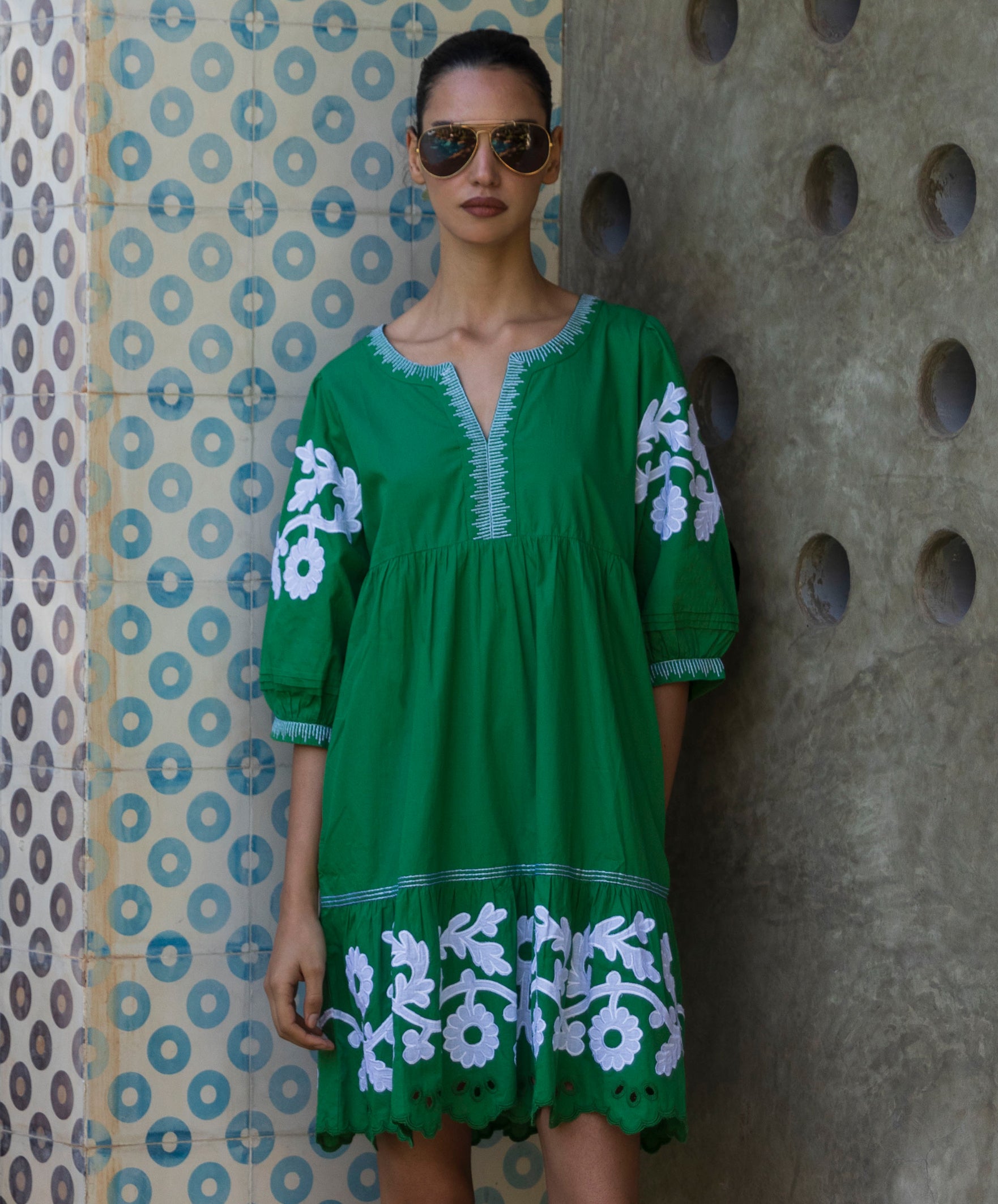 Woman wearing a green Genta dress with white floral patterns against a textured wall.